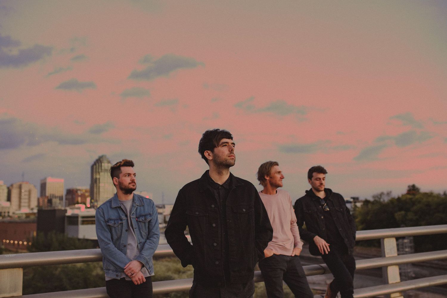 Band members standing together at sunset with city skyline visible in background.