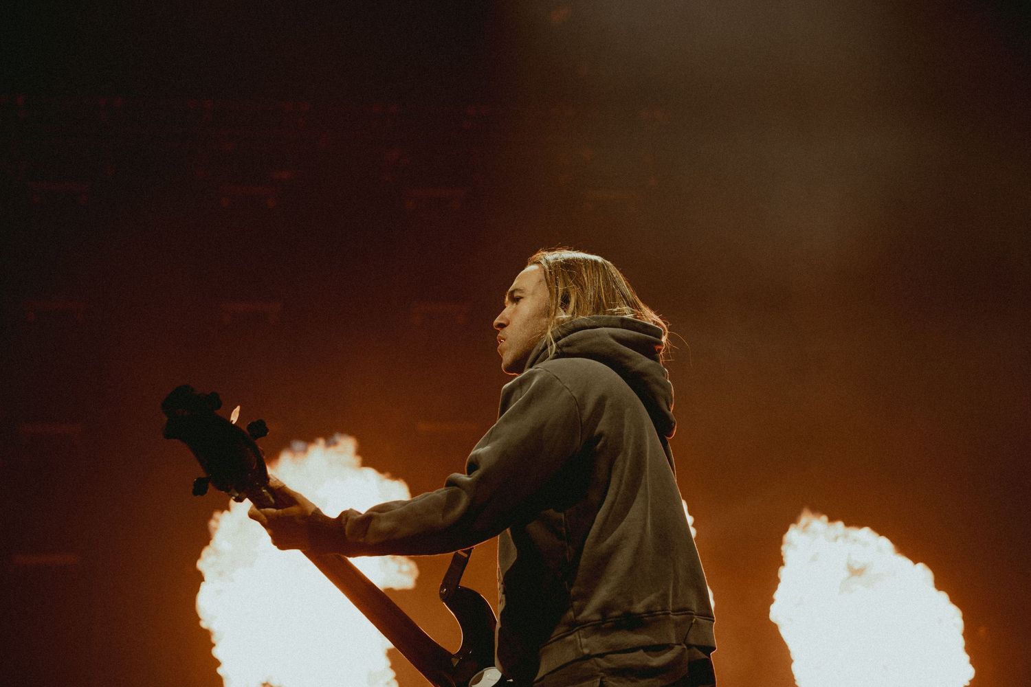 Musician plays guitar silhouetted against bright flames during concert performance.