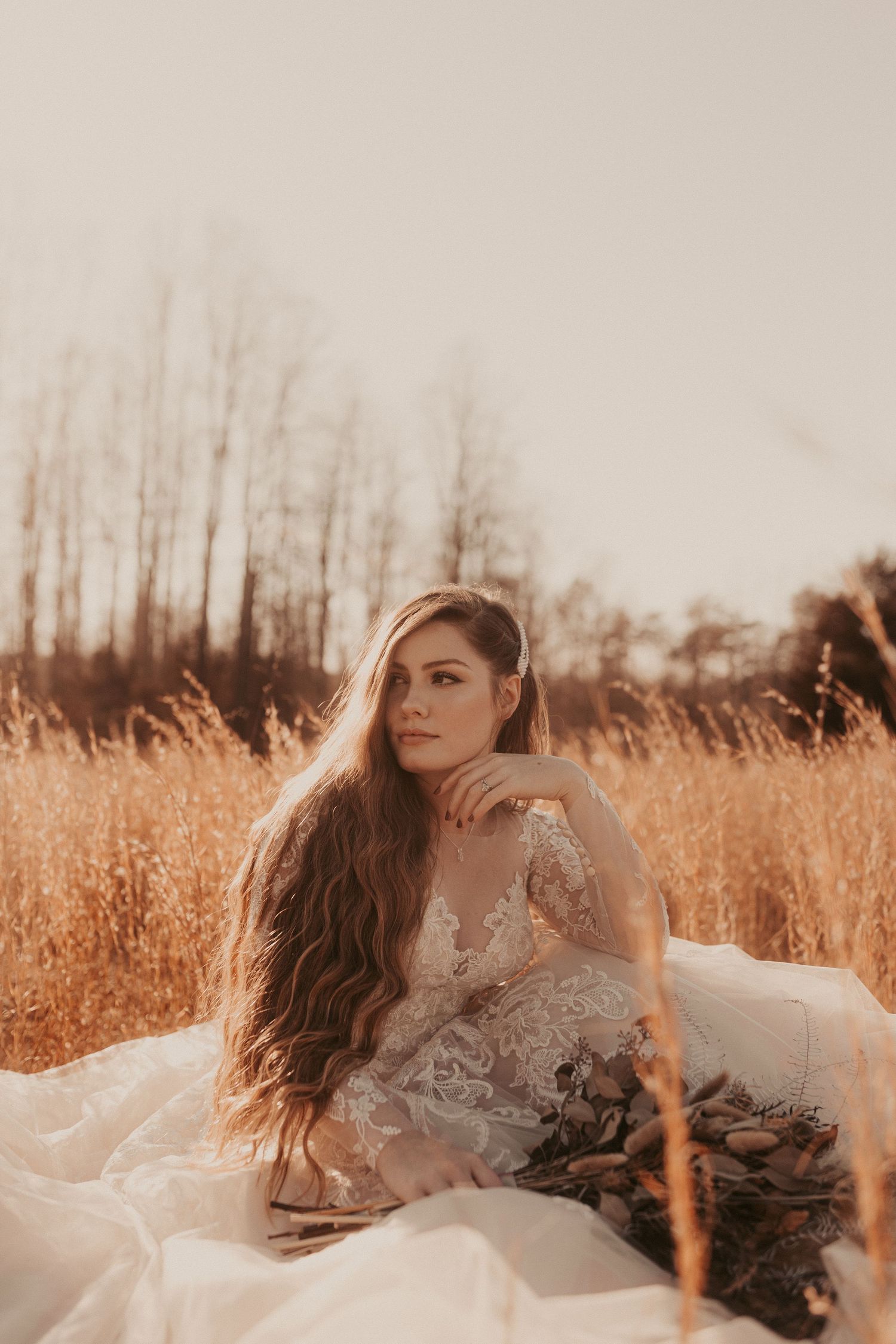 Ethereal bridal portrait in a golden field during sunset with flowing lace dress.