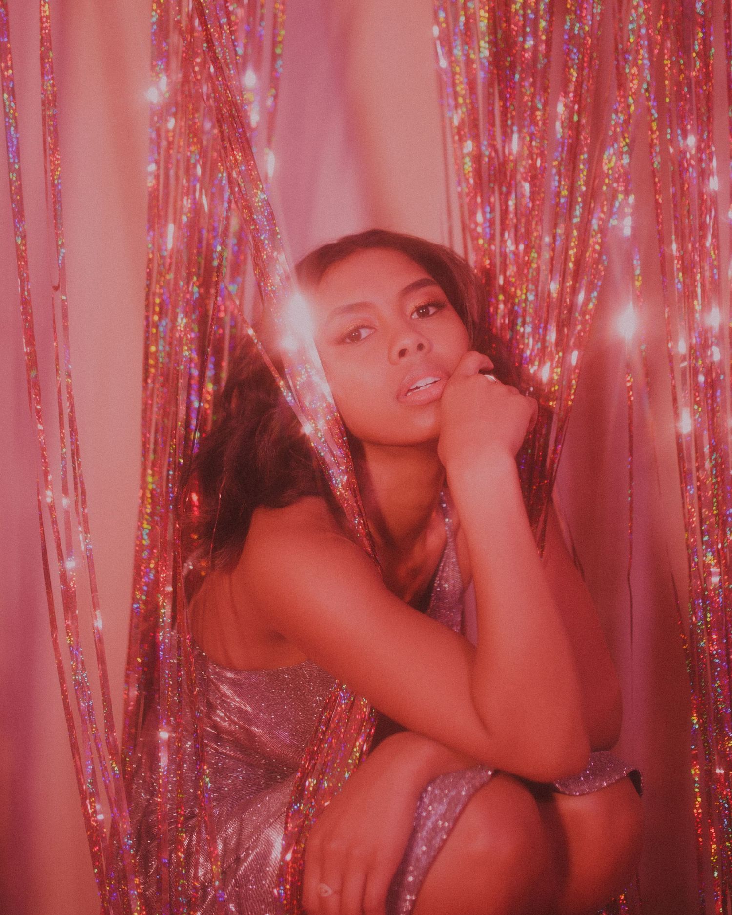 Glamorous fashion photo with sparkly pink tinsel backdrop and dramatic lighting.