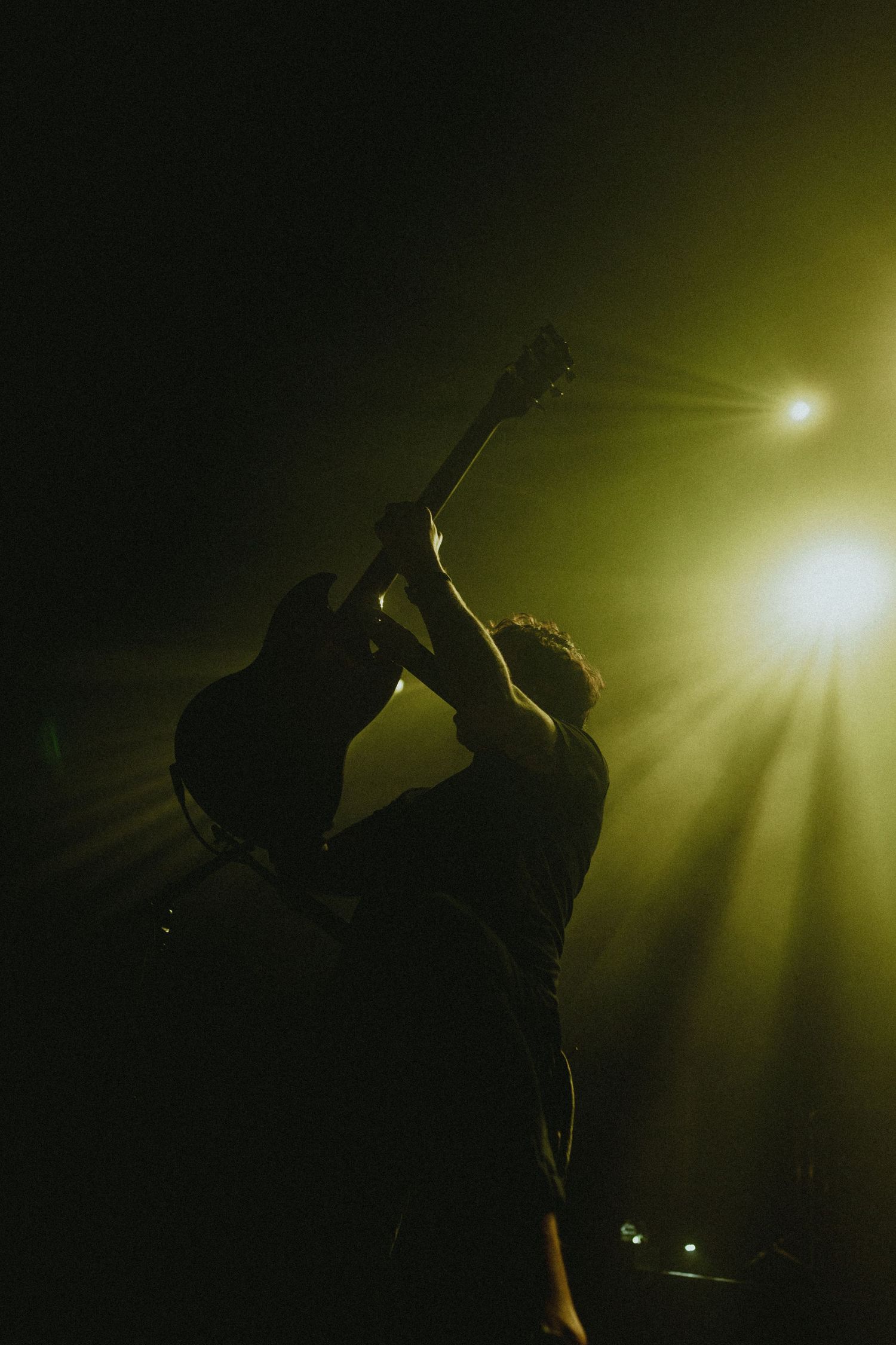 Dramatic silhouette of guitarist performing under bright yellow stage lighting.