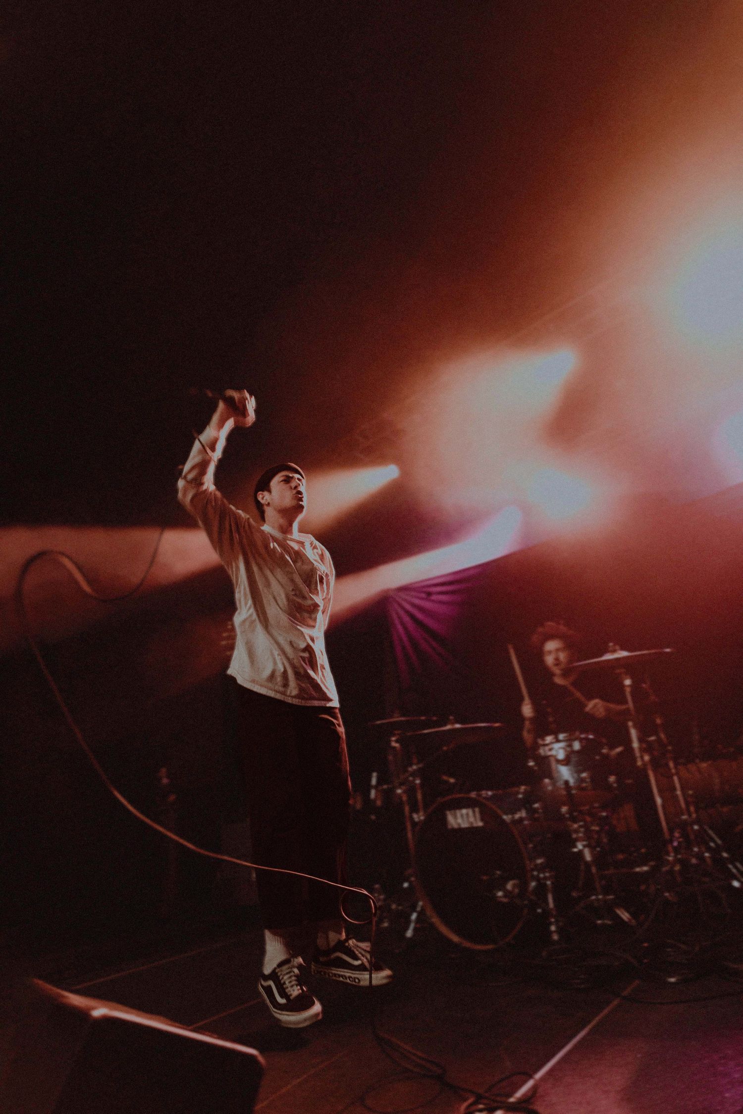 A silhouetted performer leaps energetically across a dramatically lit concert stage.