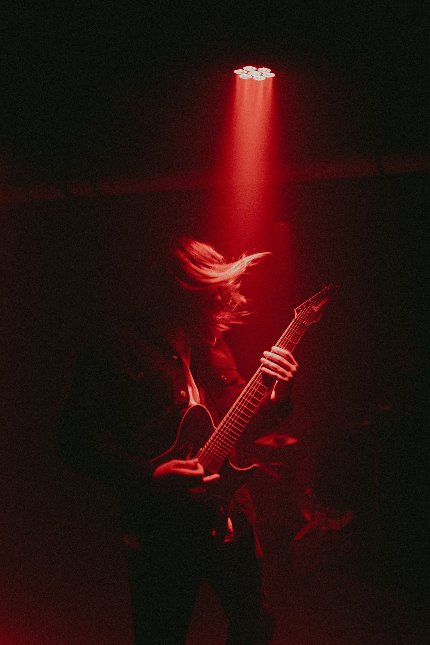 Guitarist performing under dramatic red spotlight in dark atmosphere.