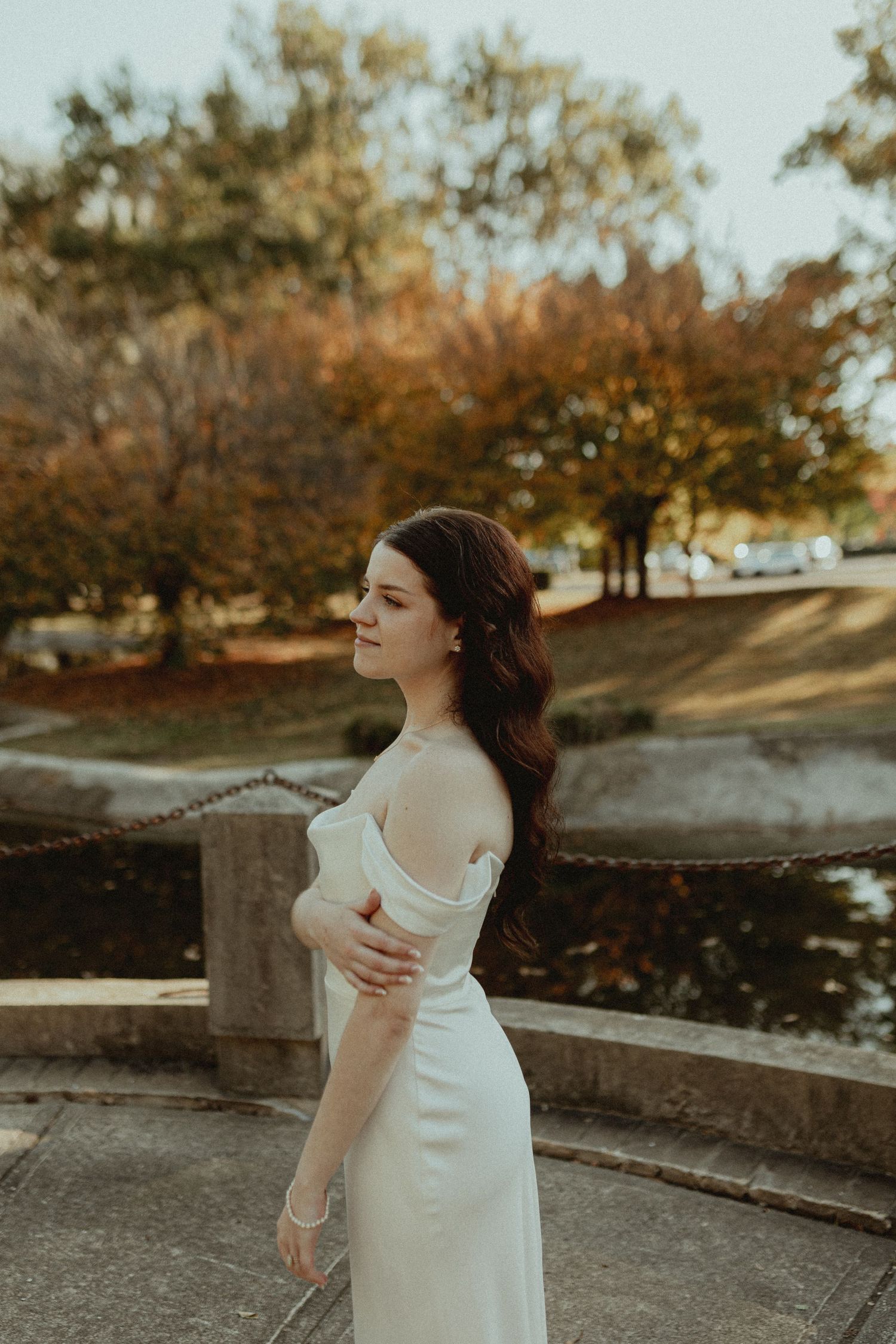 Bride in elegant white dress poses gracefully against an autumn outdoor setting.