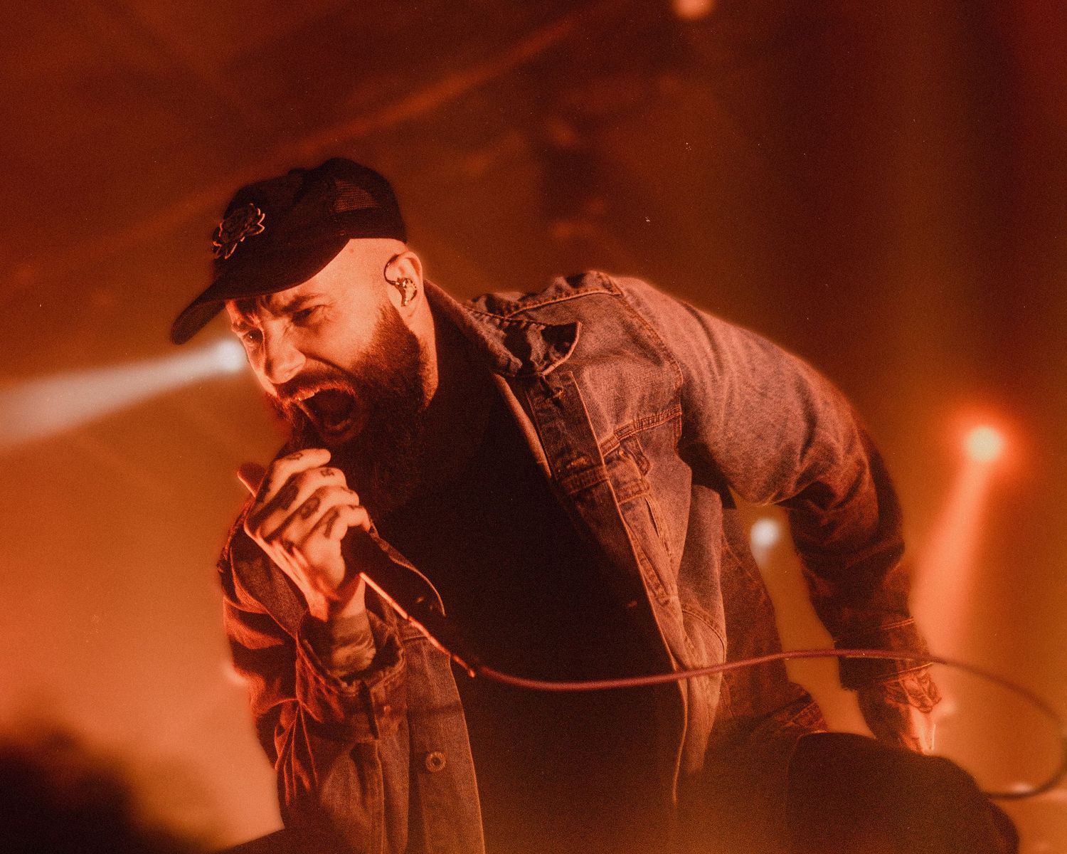 Singer performs passionately on stage wearing cap and jacket with dramatic lighting.