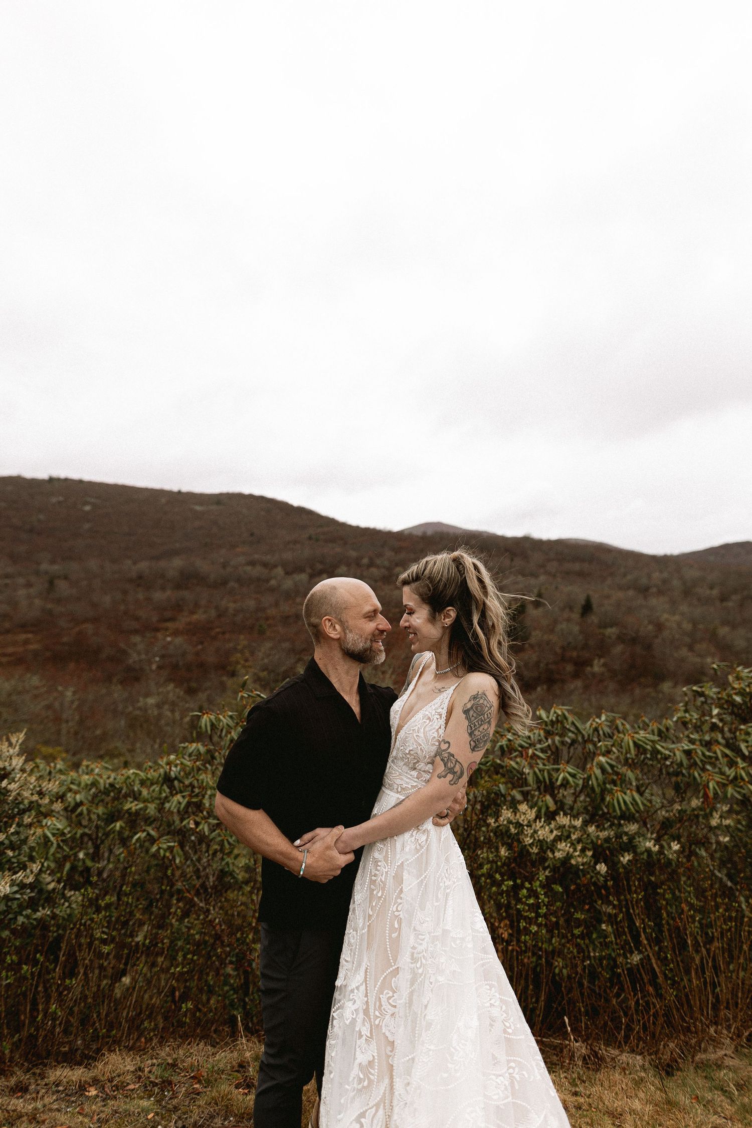 A couple shares an intimate moment against a backdrop of rolling hills and cloudy skies.