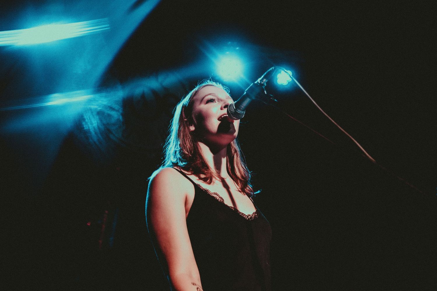 Singer performs on dark stage with dramatic blue lighting.