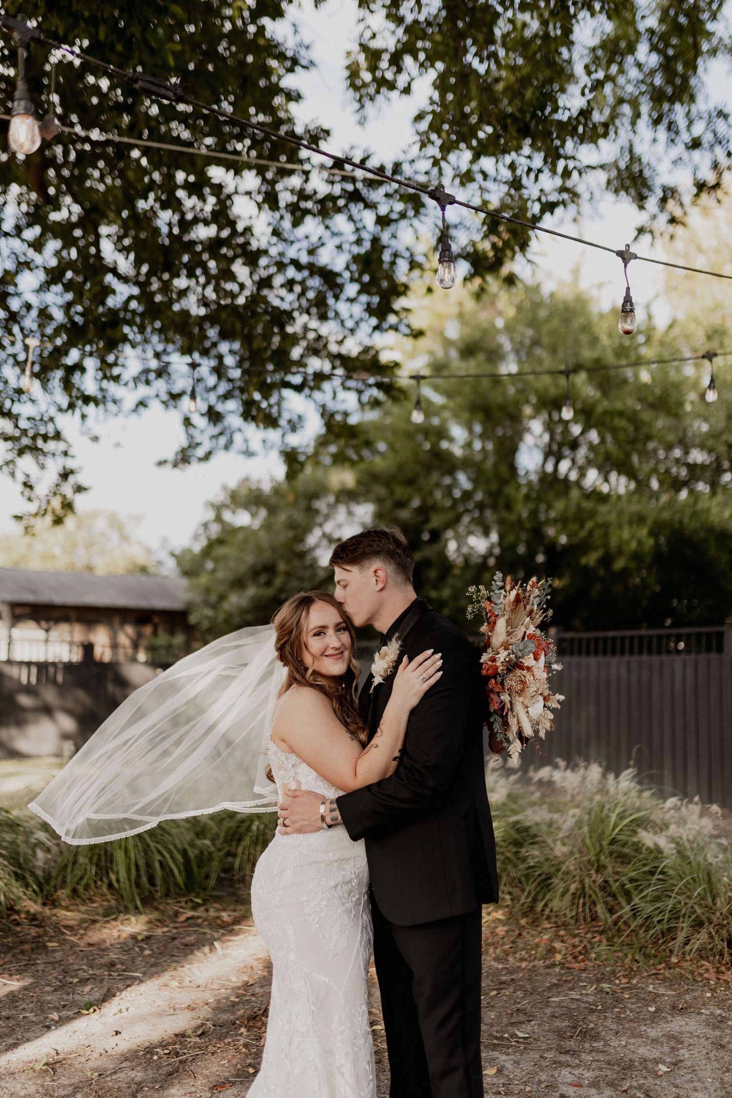 Romantic outdoor wedding portrait with flowing veil and natural backdrop.