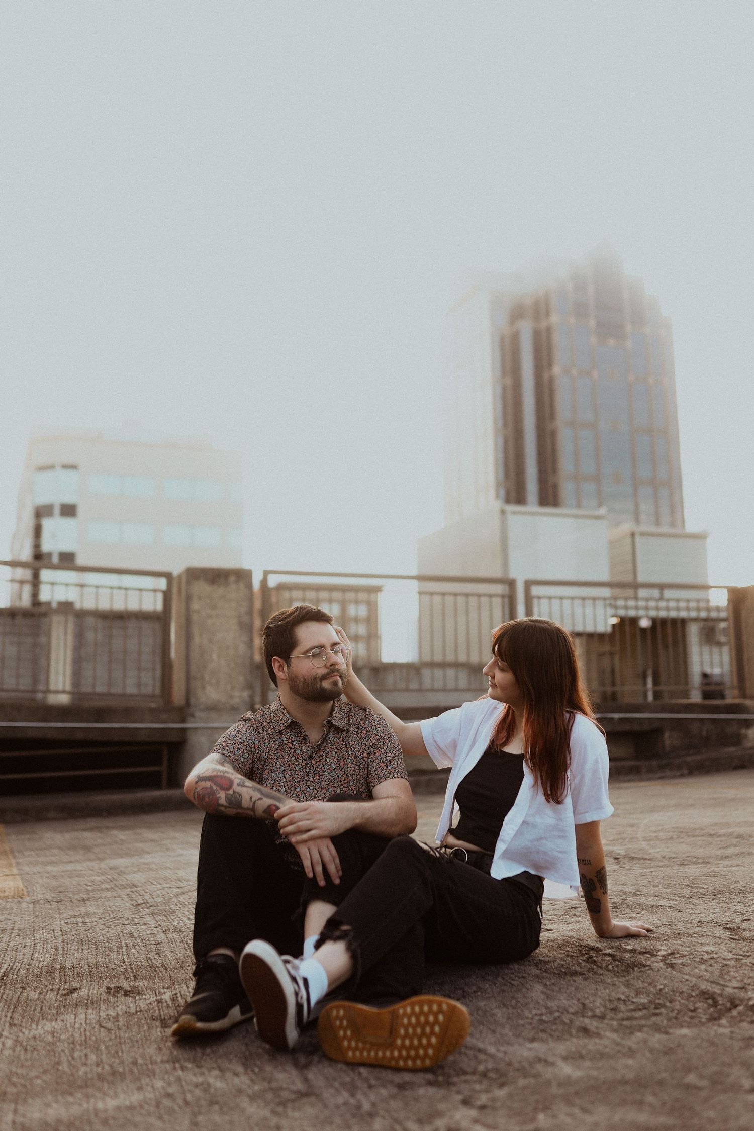 A couple enjoys a playful conversation while relaxing on a rooftop with city views.