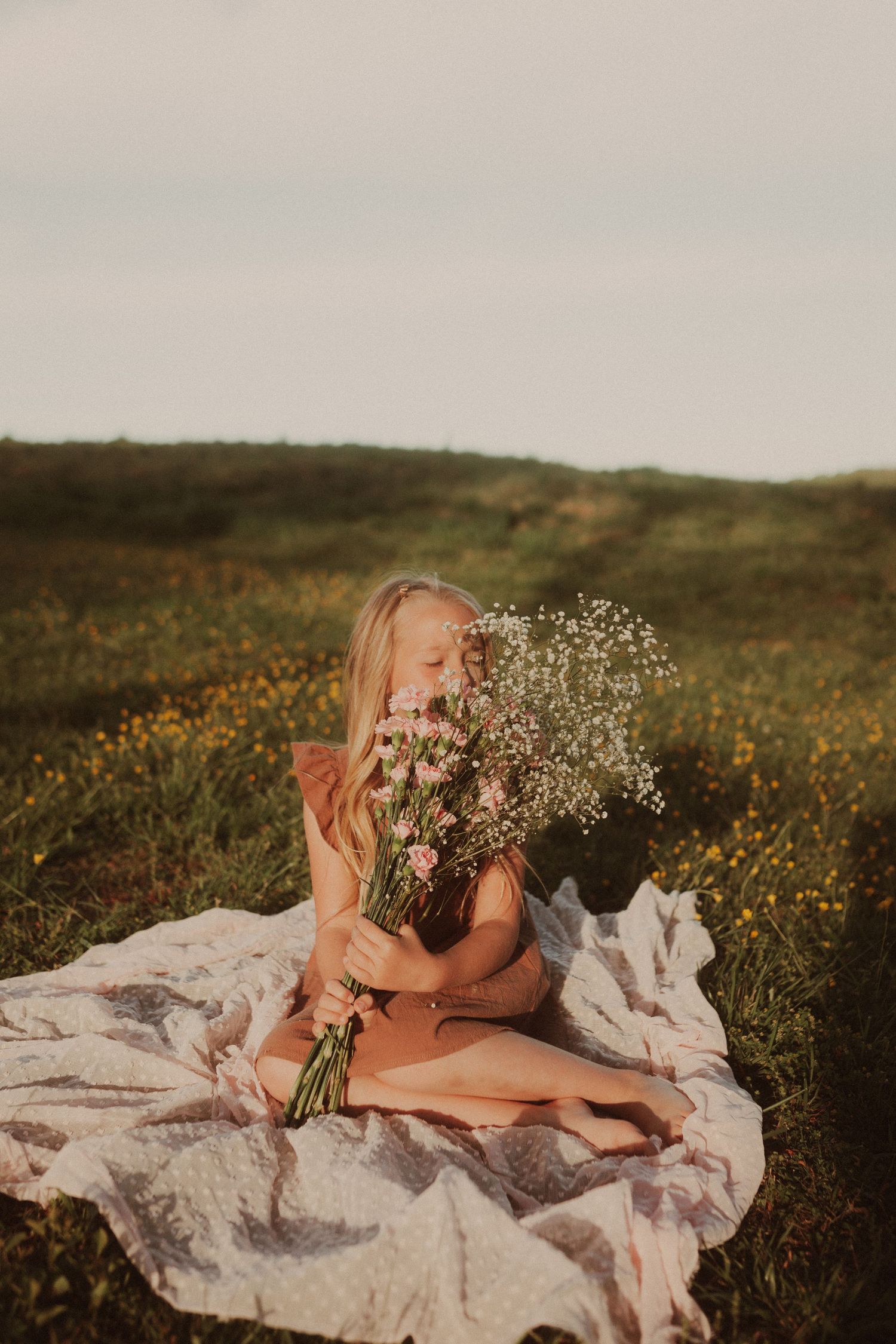 Person poses with wildflower bouquet on white blanket in meadow.