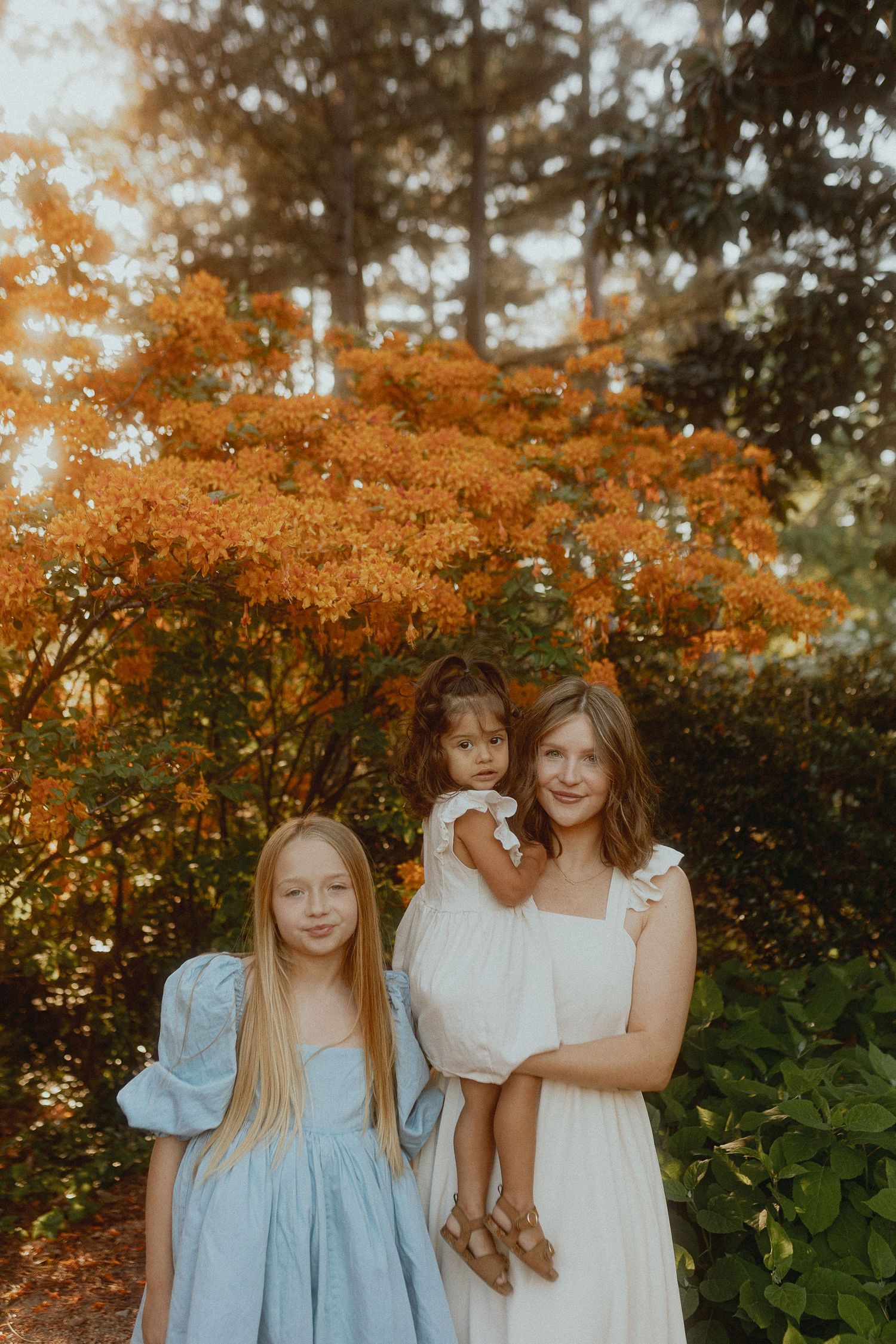 Children in blue and white dresses pose together among vibrant orange autumn foliage.