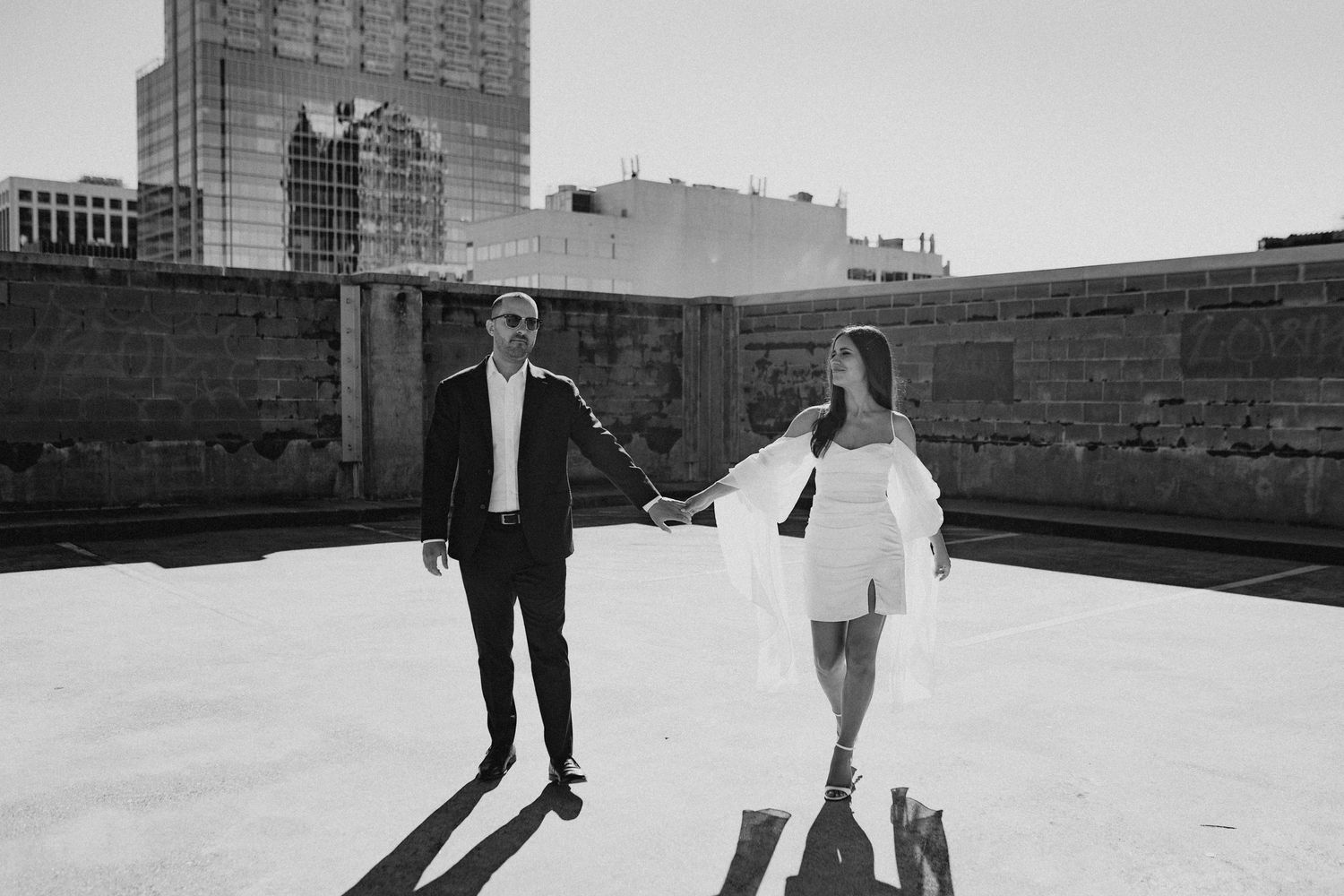 Couple walking together on urban rooftop with city skyline in background.