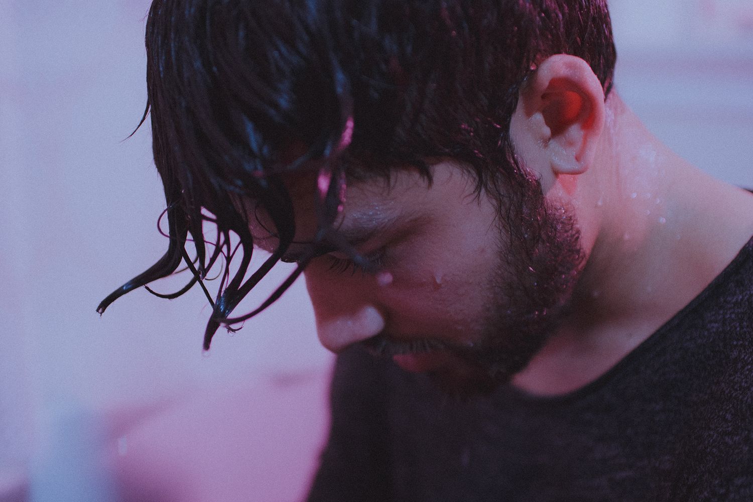 Moody close-up portrait with wet hair against purple-tinted background.