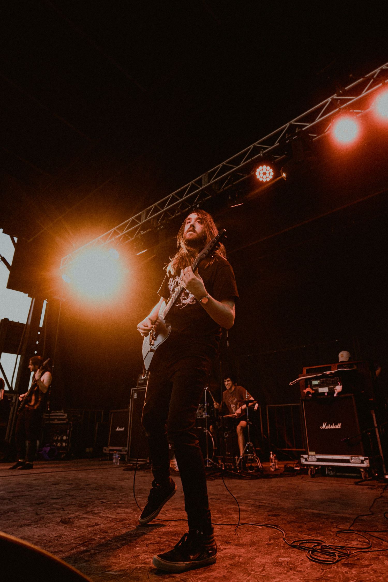 Musician playing guitar on stage with warm orange stage lighting and equipment visible.