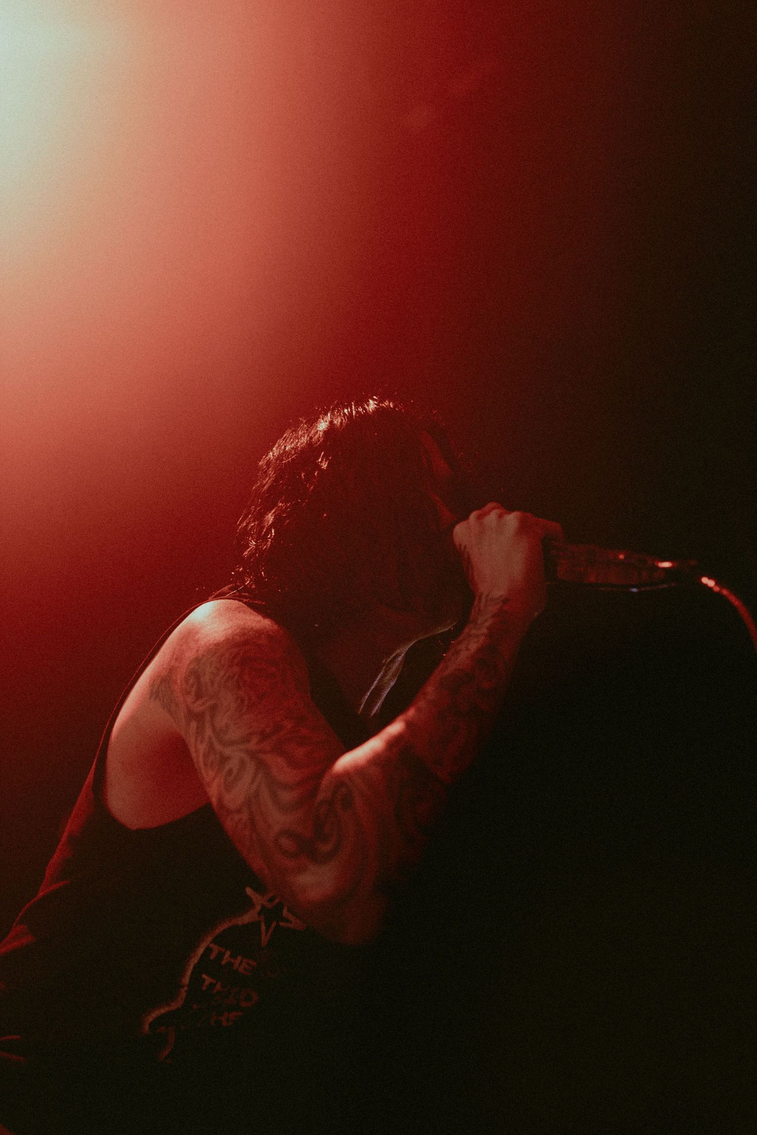 Performer singing into microphone under red stage lighting.