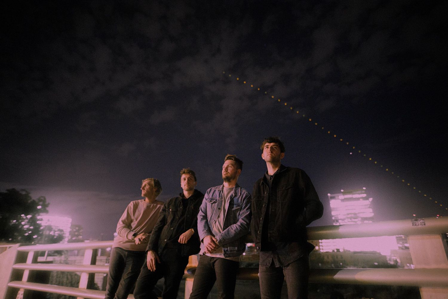 A group of people sit on a bench against a dark sky with stars and purple lighting in the background.
