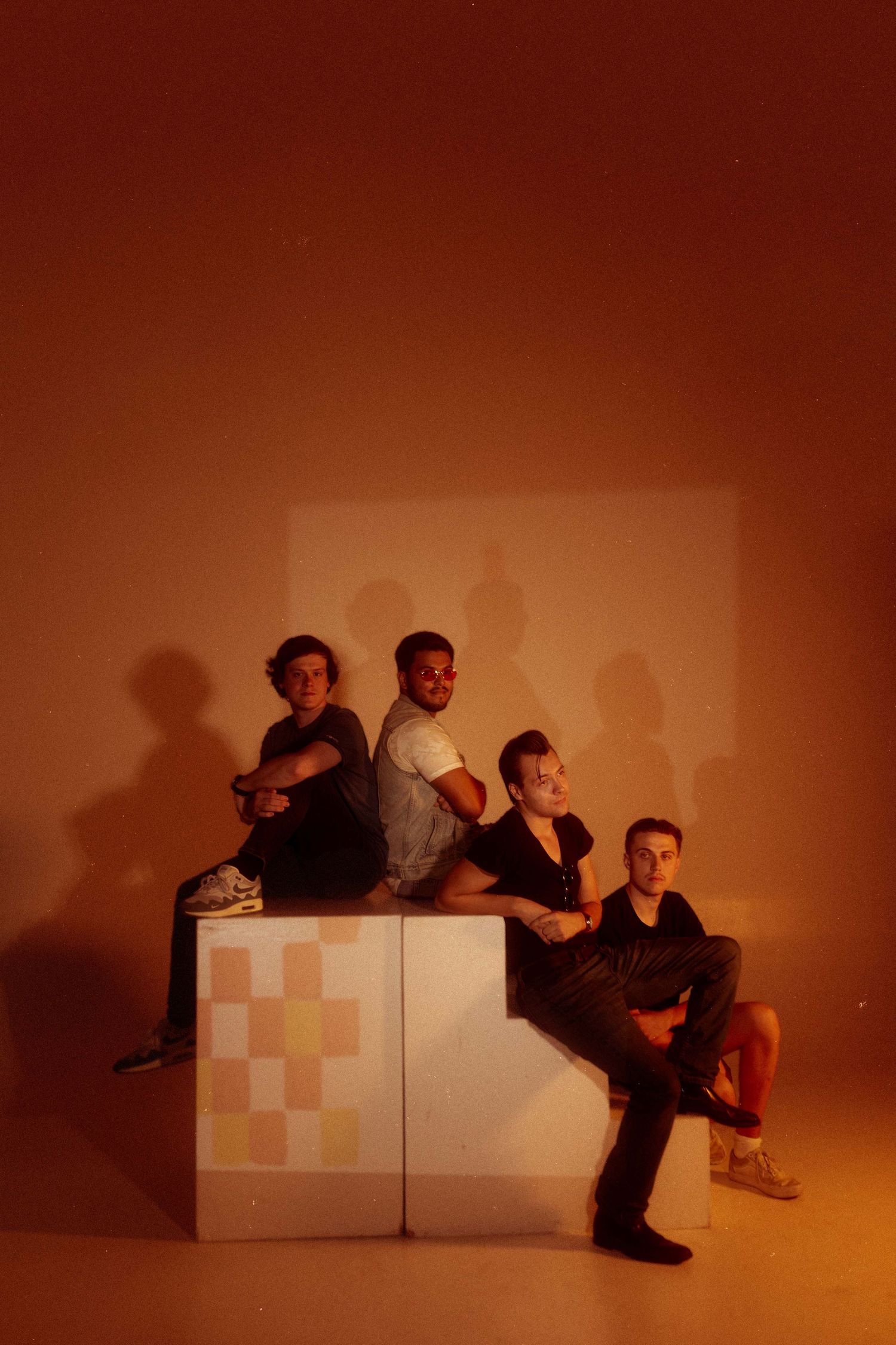 Group poses on geometric blocks against orange backdrop with dramatic shadows.