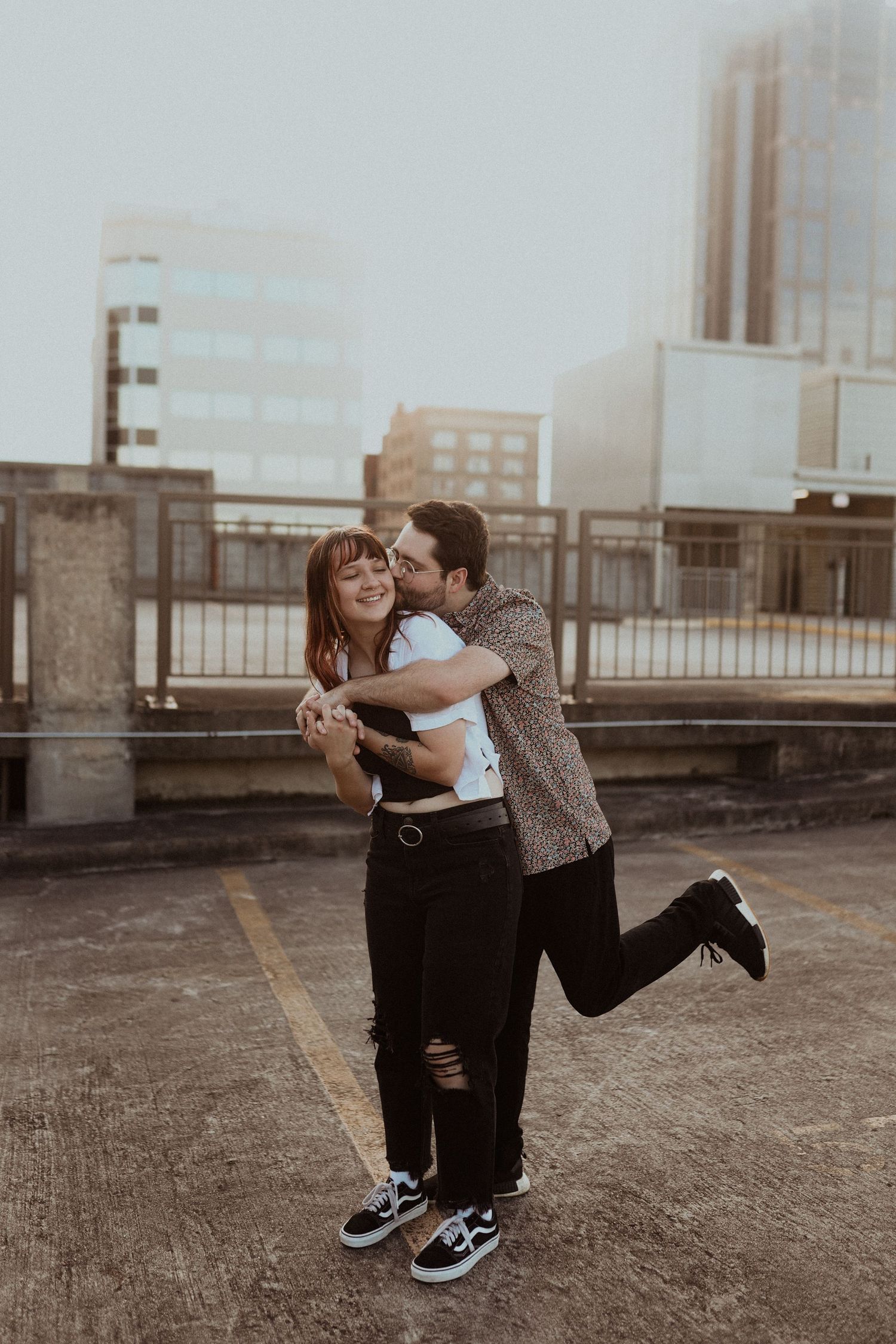 Two people dance and spin together on a rooftop parking area with downtown buildings visible.