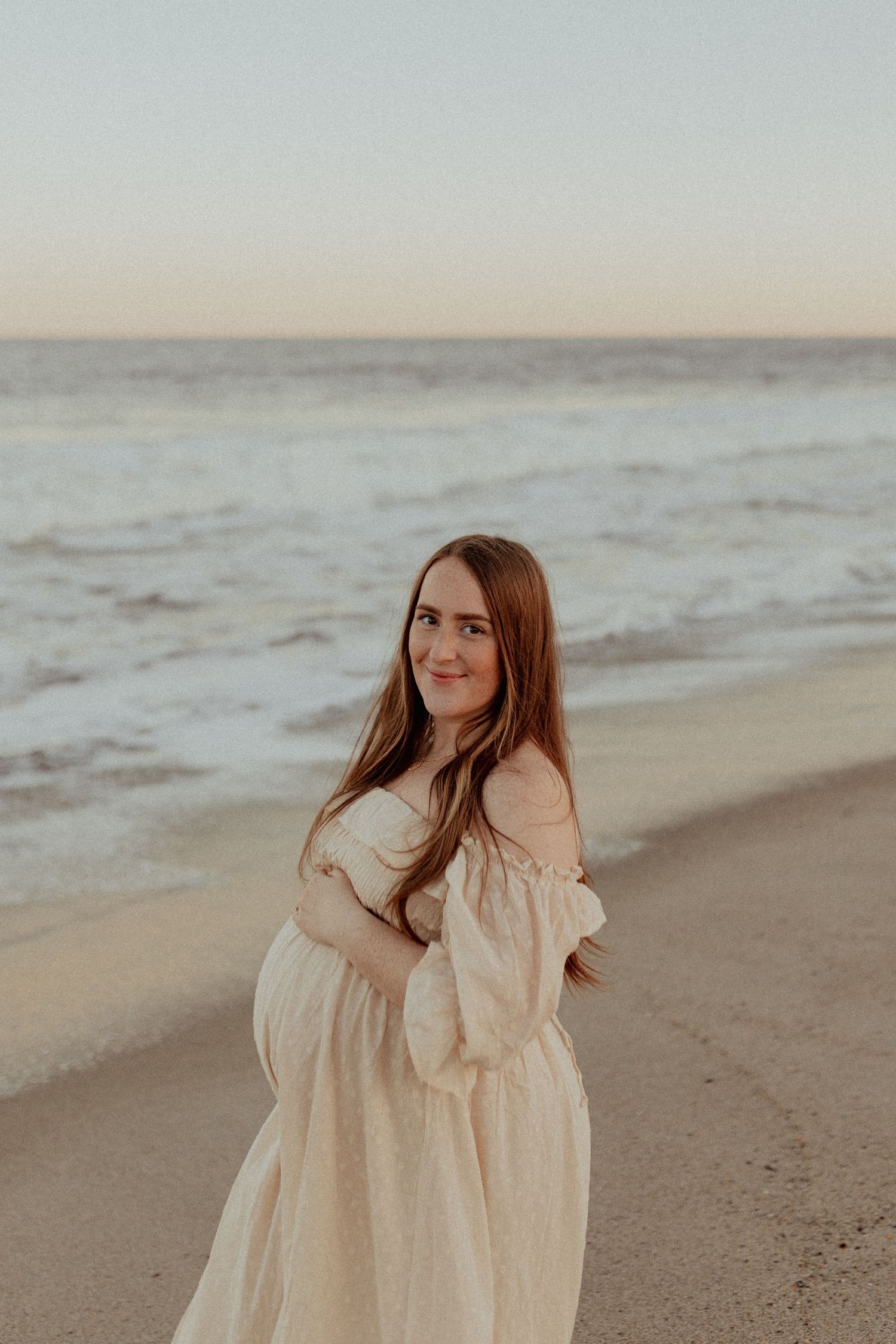 A light and airy beach photoshoot featuring flowing cream dress against a misty ocean backdrop.