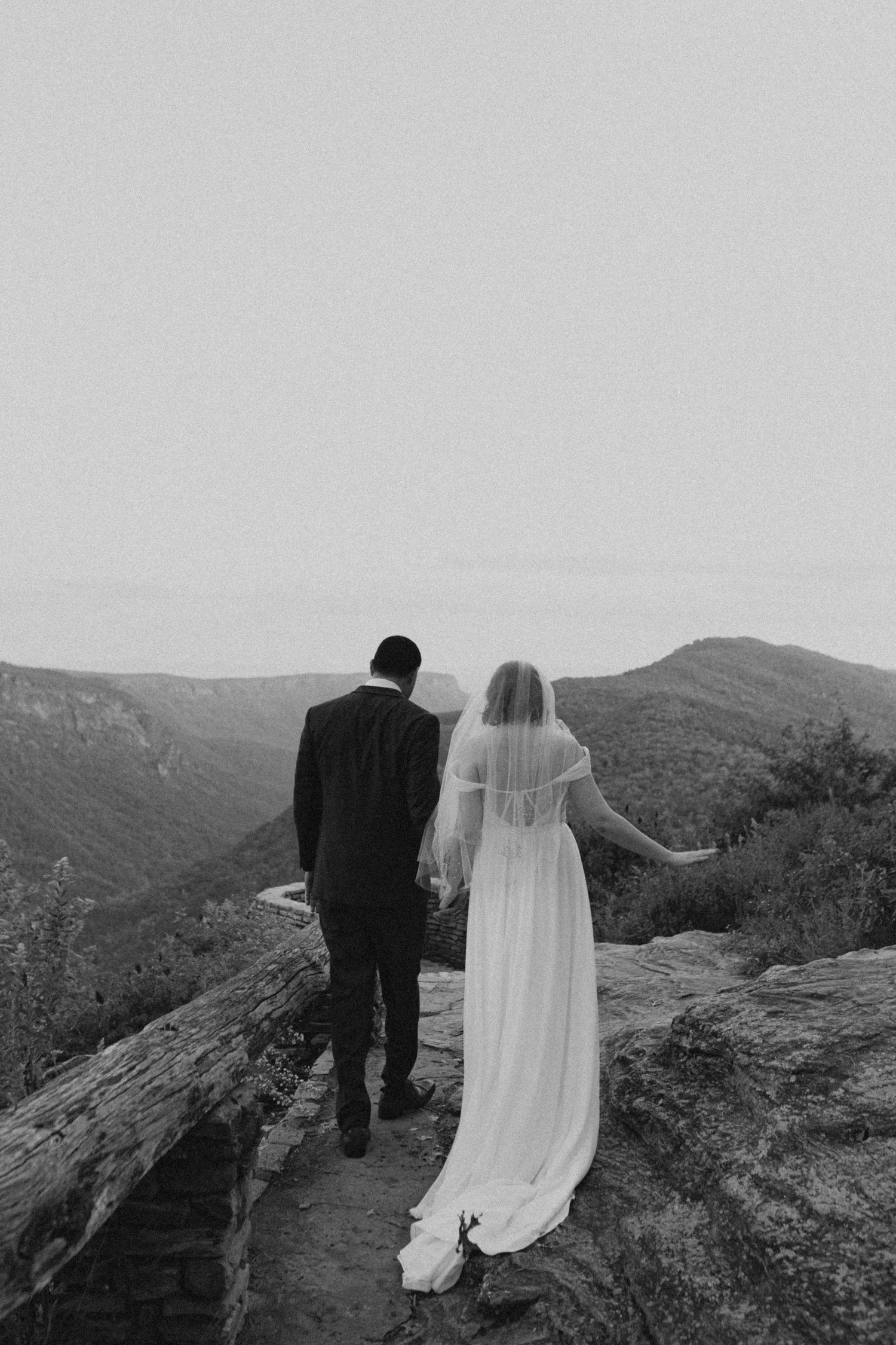 A couple walks along a mountain path in black and white wedding photography.