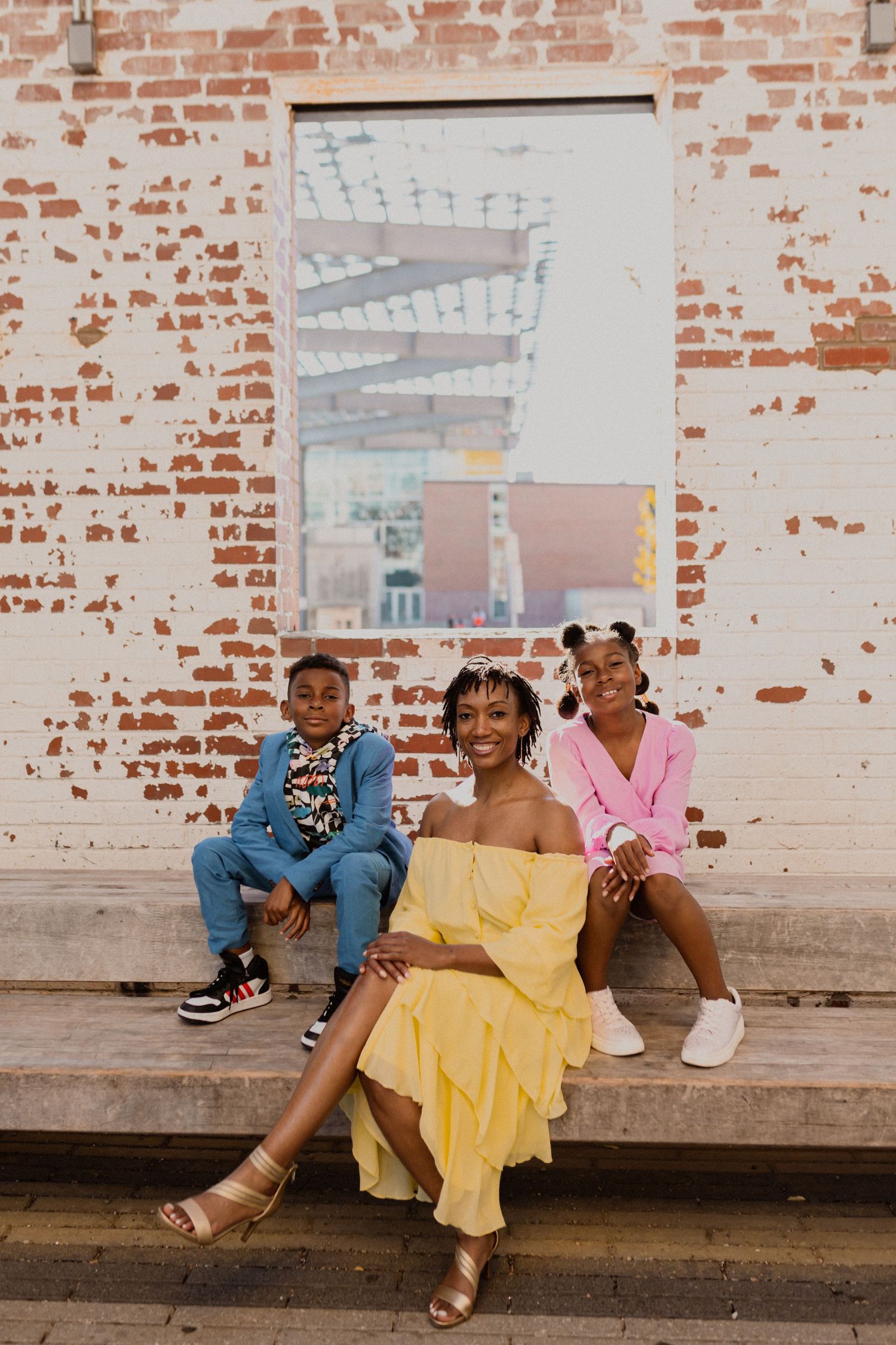 Group seated on yellow fabric against industrial brick wall in artistic setting.