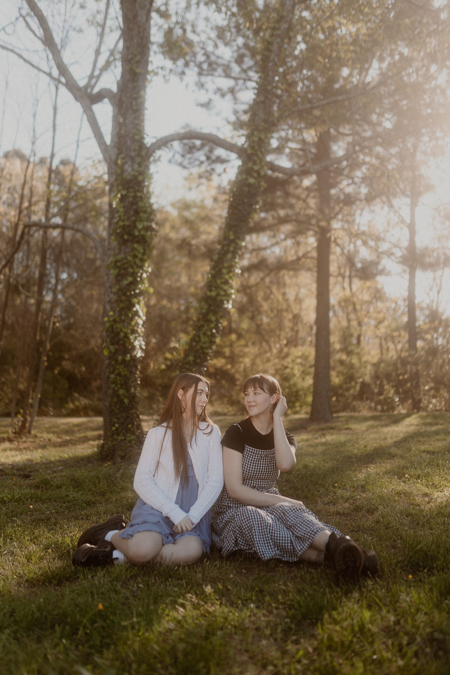 A dreamy forest photoshoot with people lounging on grass in soft sunlight.