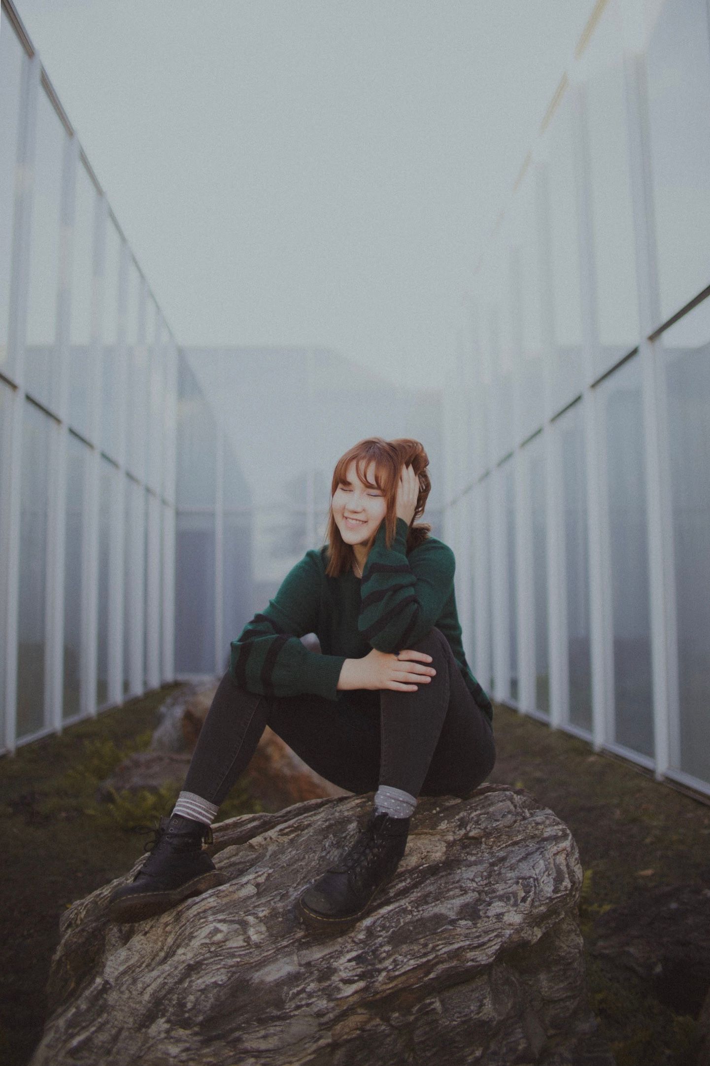 Person in green jacket sits contemplatively on rock in misty corridor with white walls.