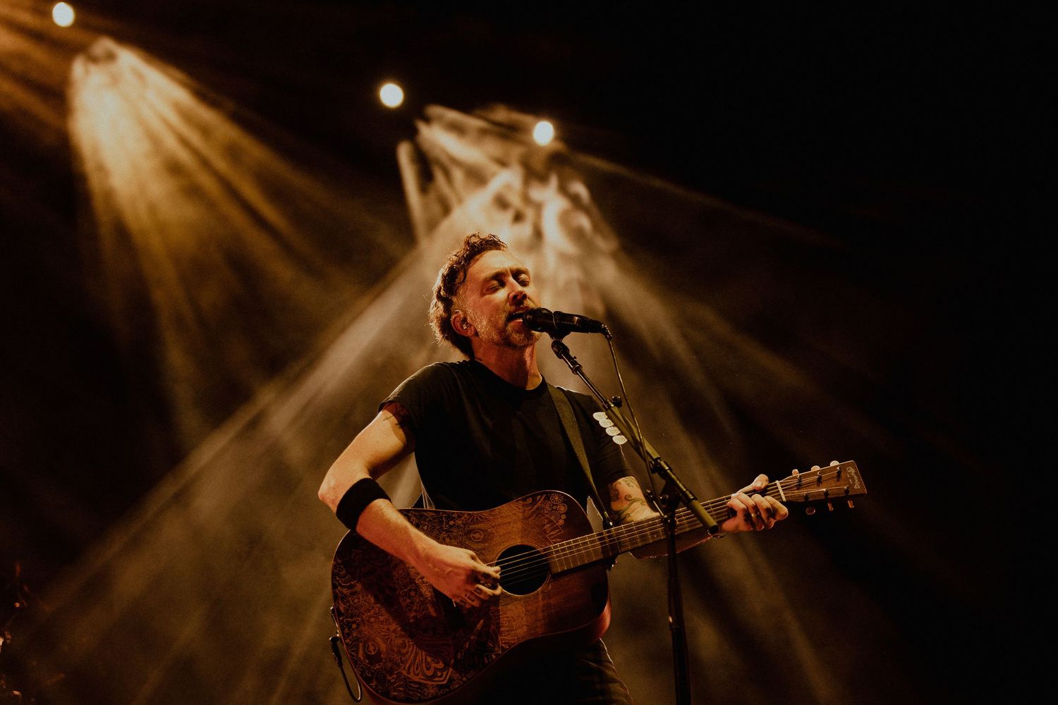 Acoustic guitarist performing under golden spotlights on dark stage.