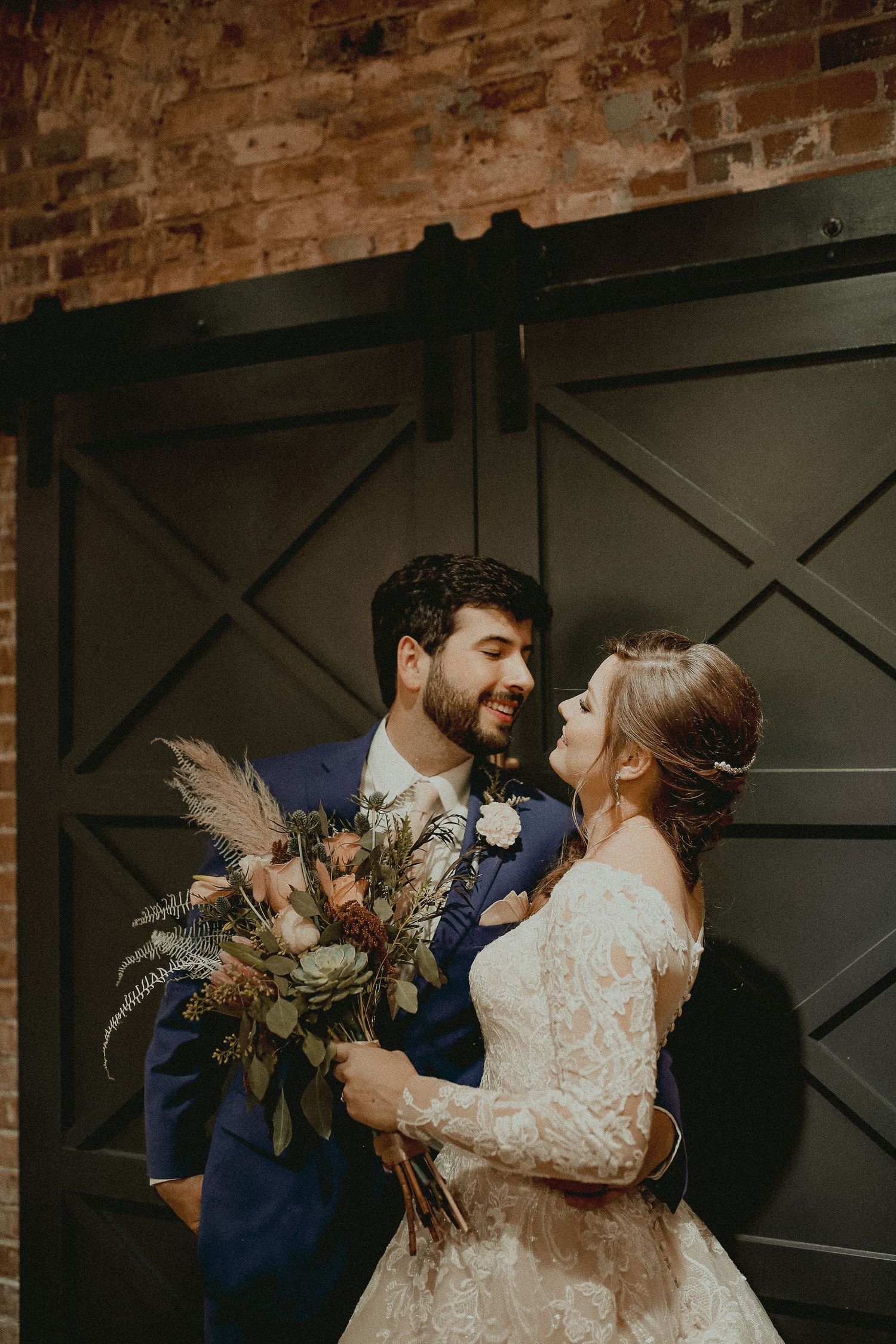 A couple shares an intimate dance moment in front of a rustic brick wall at their wedding celebration.