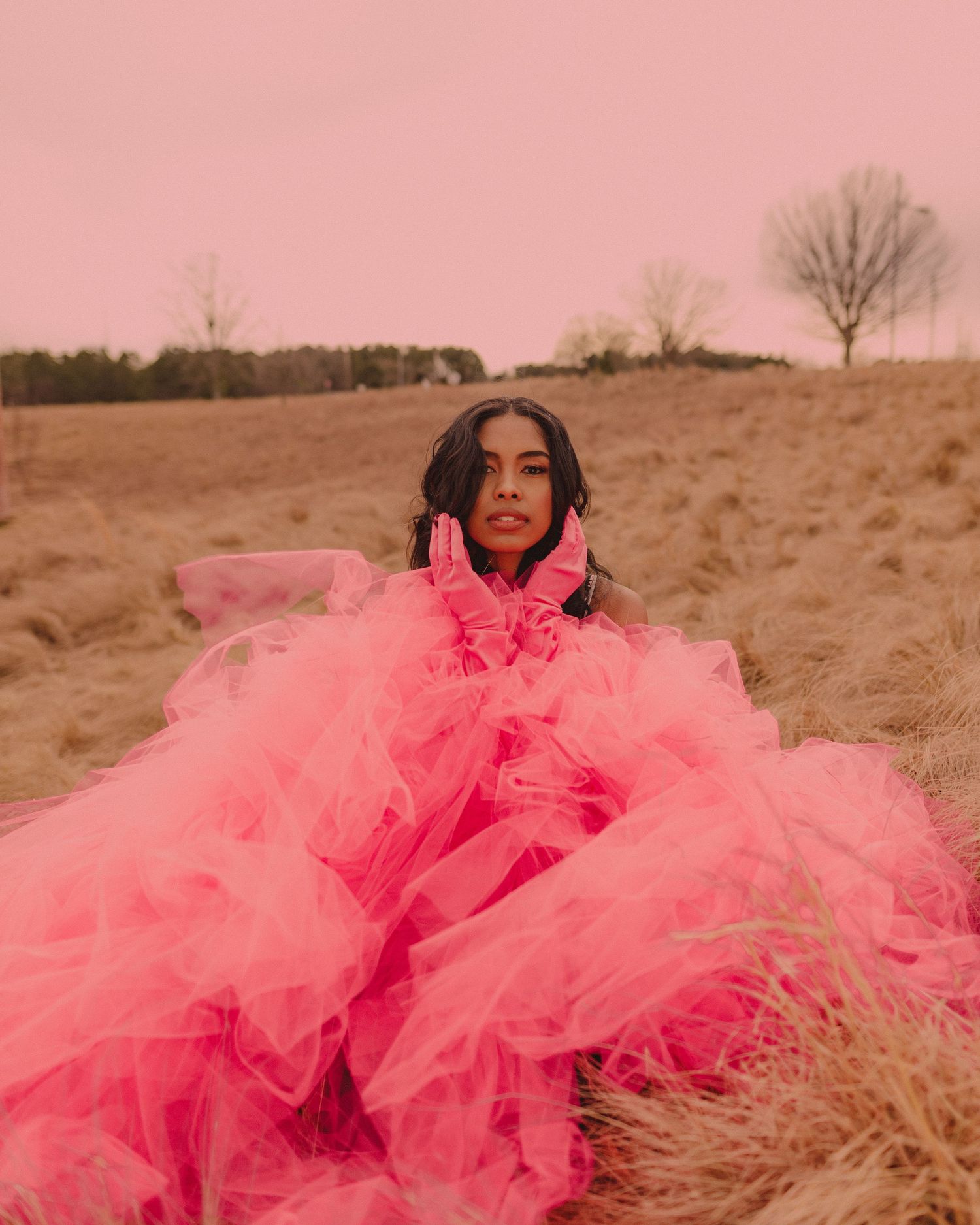Dramatic fashion shoot in a field featuring a flowing pink tulle gown against natural grass.