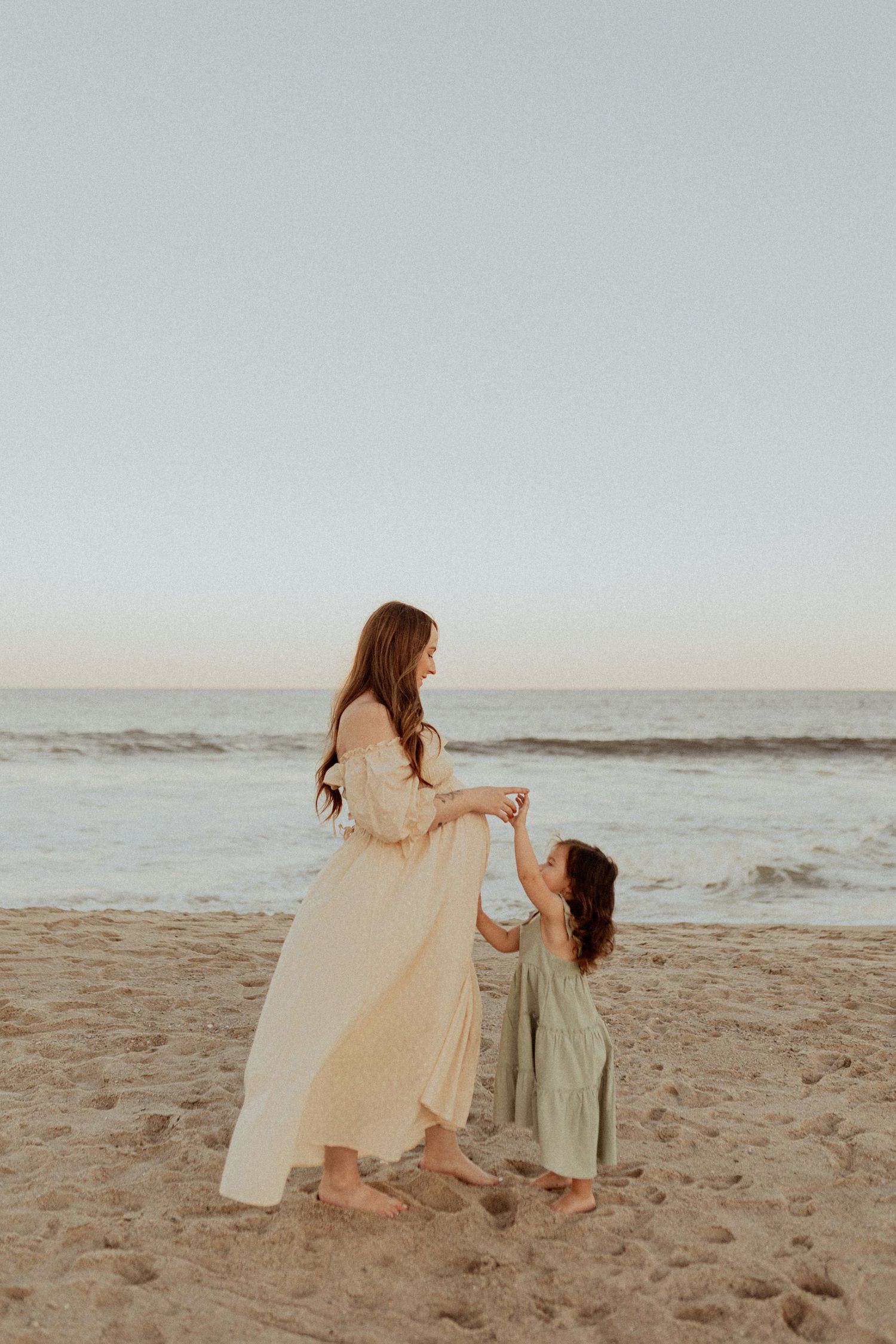A mother and child share a tender moment on a sandy beach at sunset.