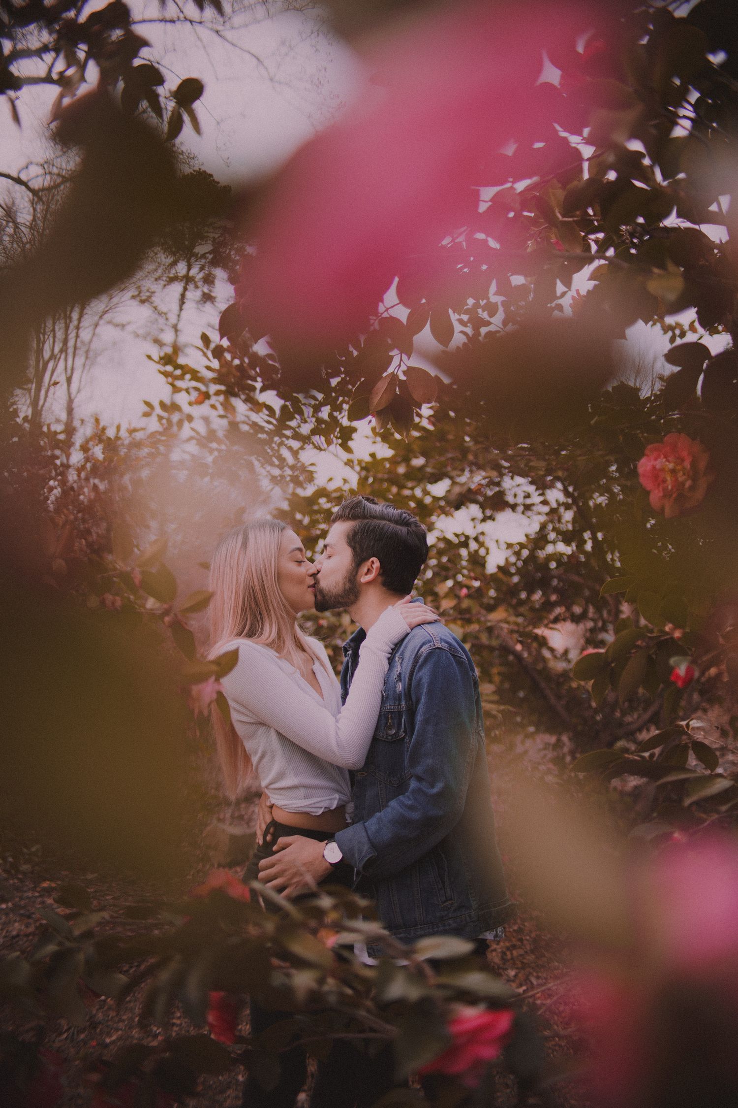 A romantic couple embraces among pink blossoms in a dreamy outdoor photoshoot.