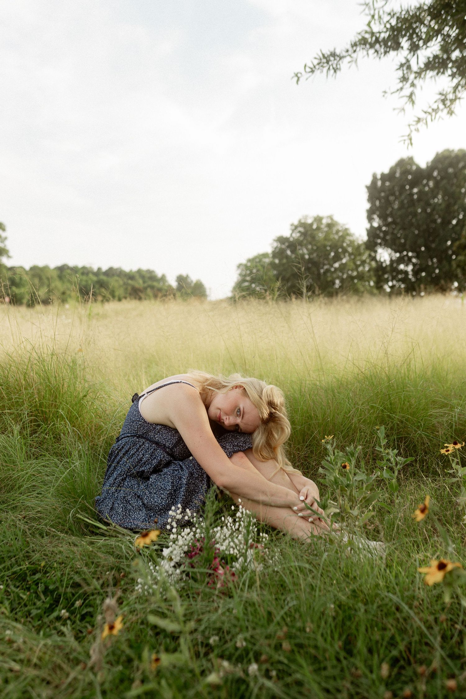 Artistic portrait in tall grass meadow with wildflowers and natural lighting.