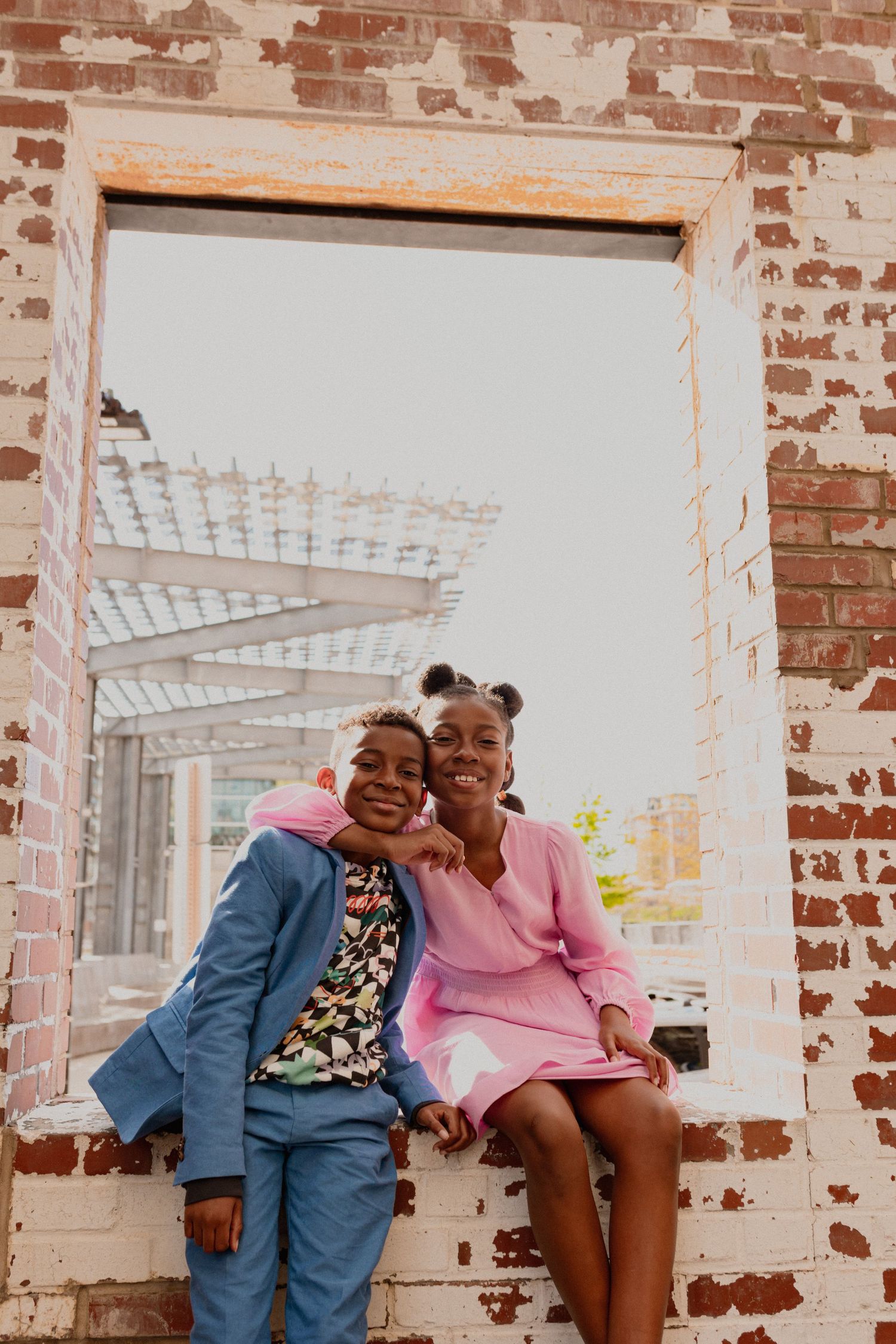 Group in colorful outfits sitting against exposed brick wall with joyful expressions.