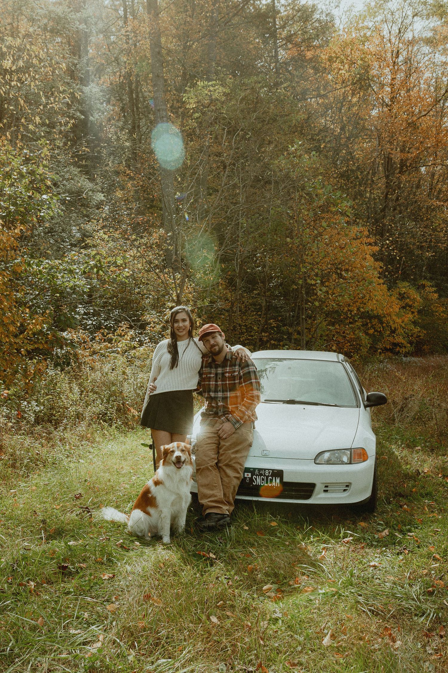 Engagement photos in autumn setting with white car and dog in background.