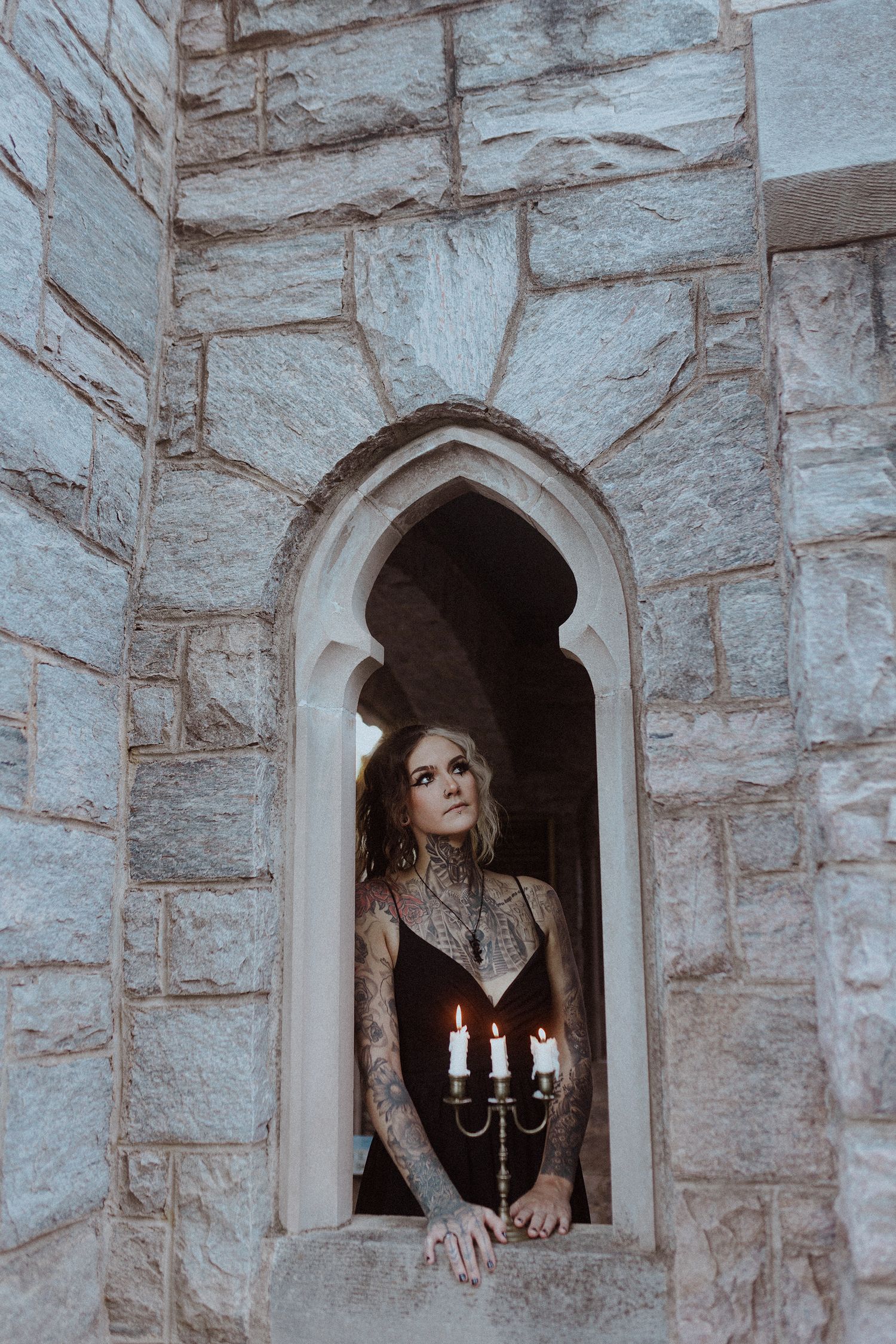 Atmospheric photos of person peering through stone castle window with candlelight.