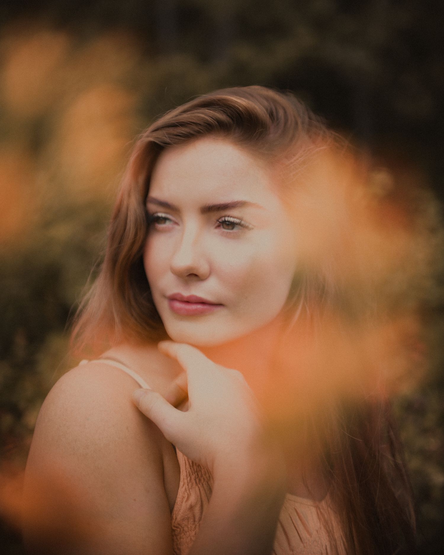 Artistic autumn portrait with selective focus and warm orange bokeh in foreground.