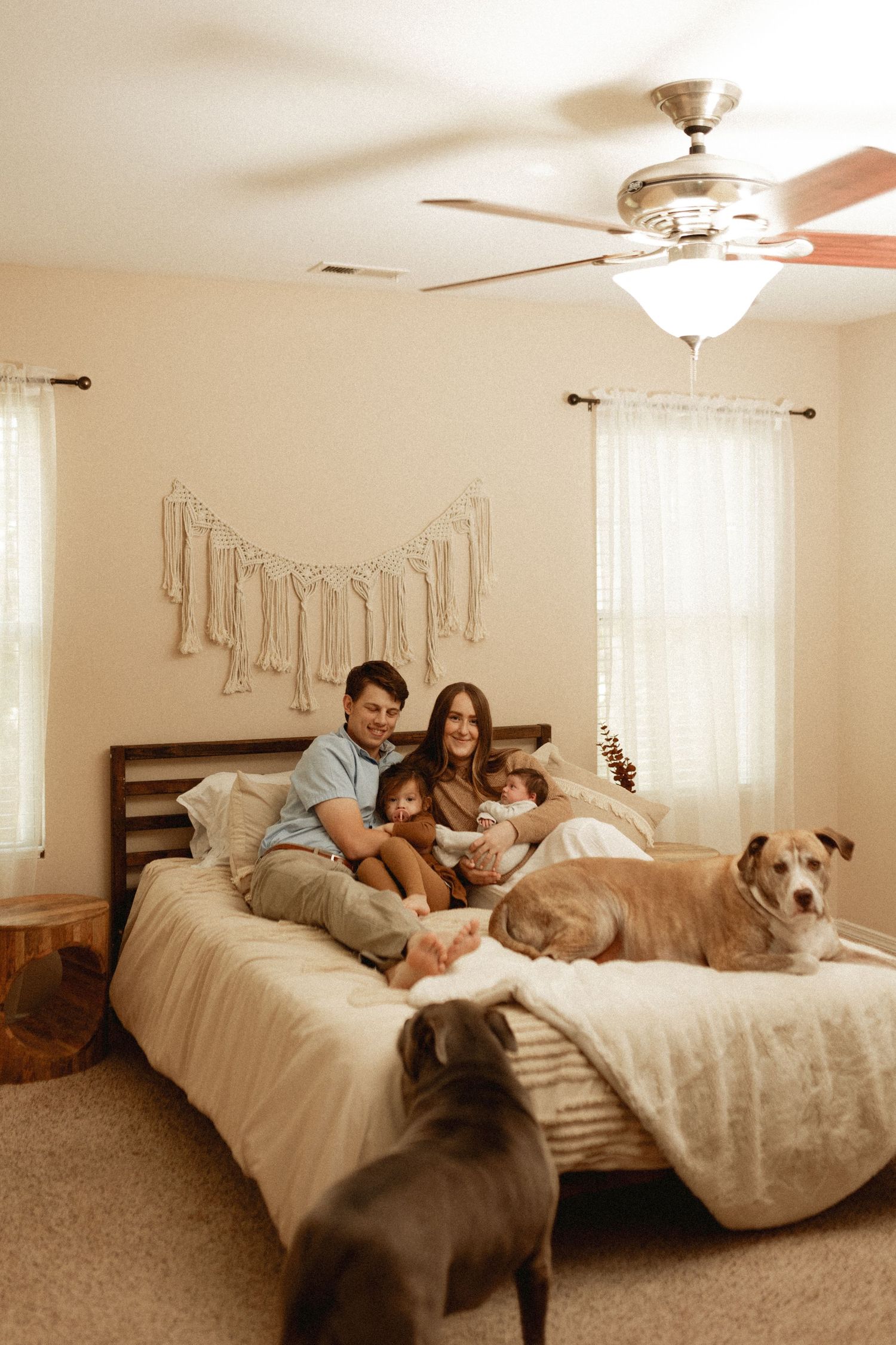 Family relaxing together on a white bed with their dog in a cozy bedroom with natural light.