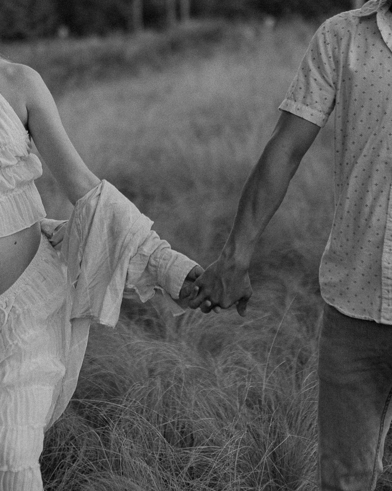 Black and white photo of hands holding in tall grass field.