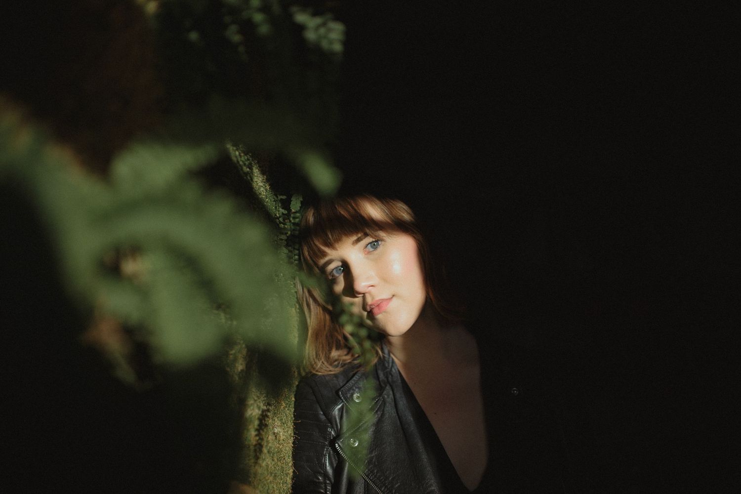 Dramatic portrait with dark shadows and natural foliage elements.