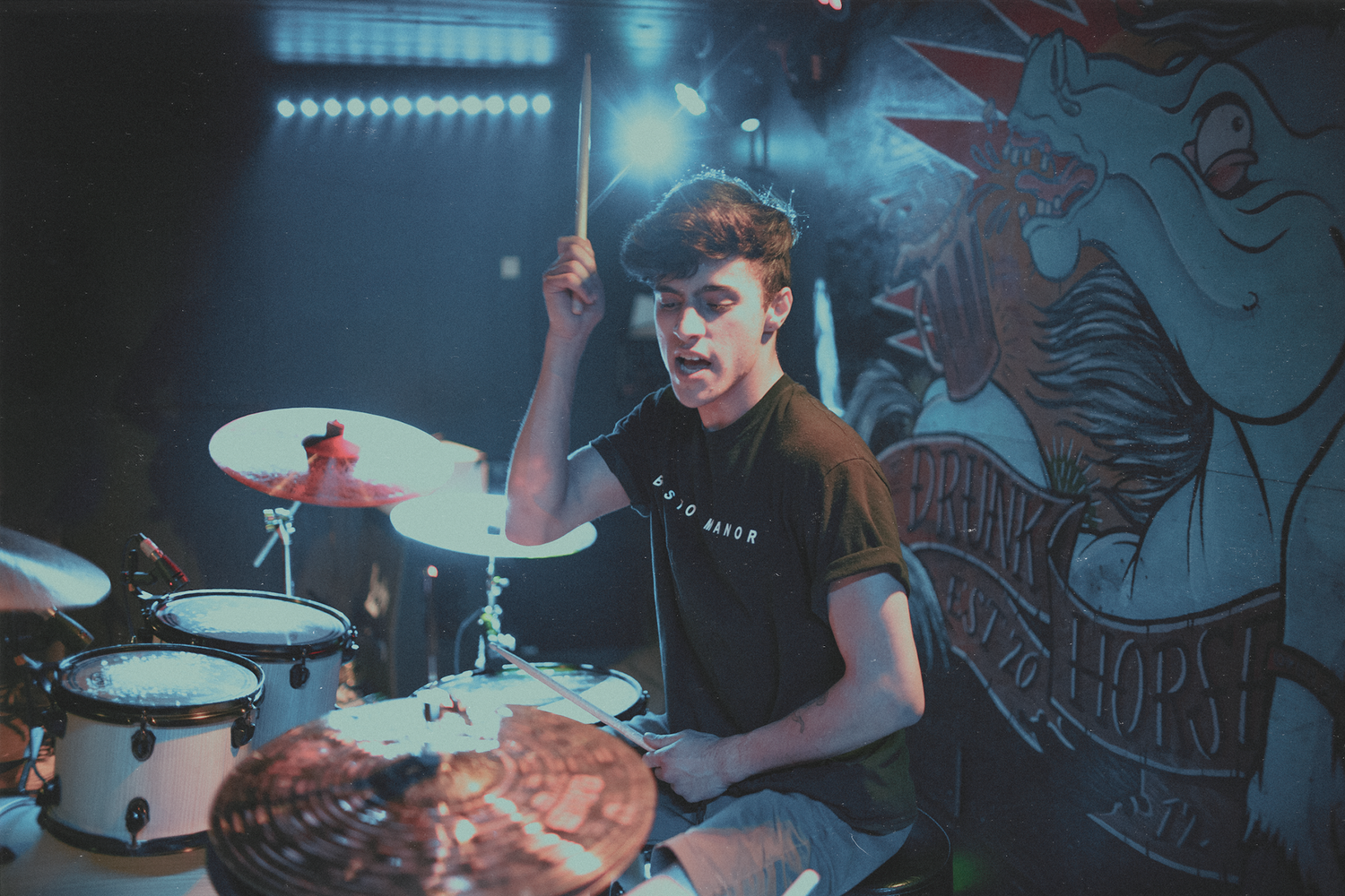 Drummer performs on stage with dramatic lighting and artistic backdrop during live music show.