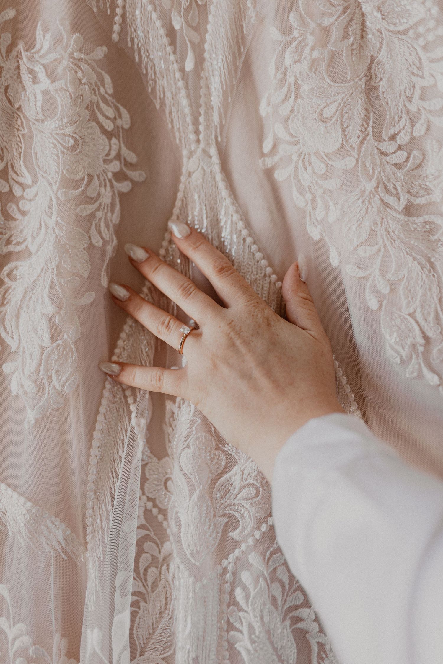 Close-up detail of intricate lace pattern on a white wedding dress with hands touching the fabric.