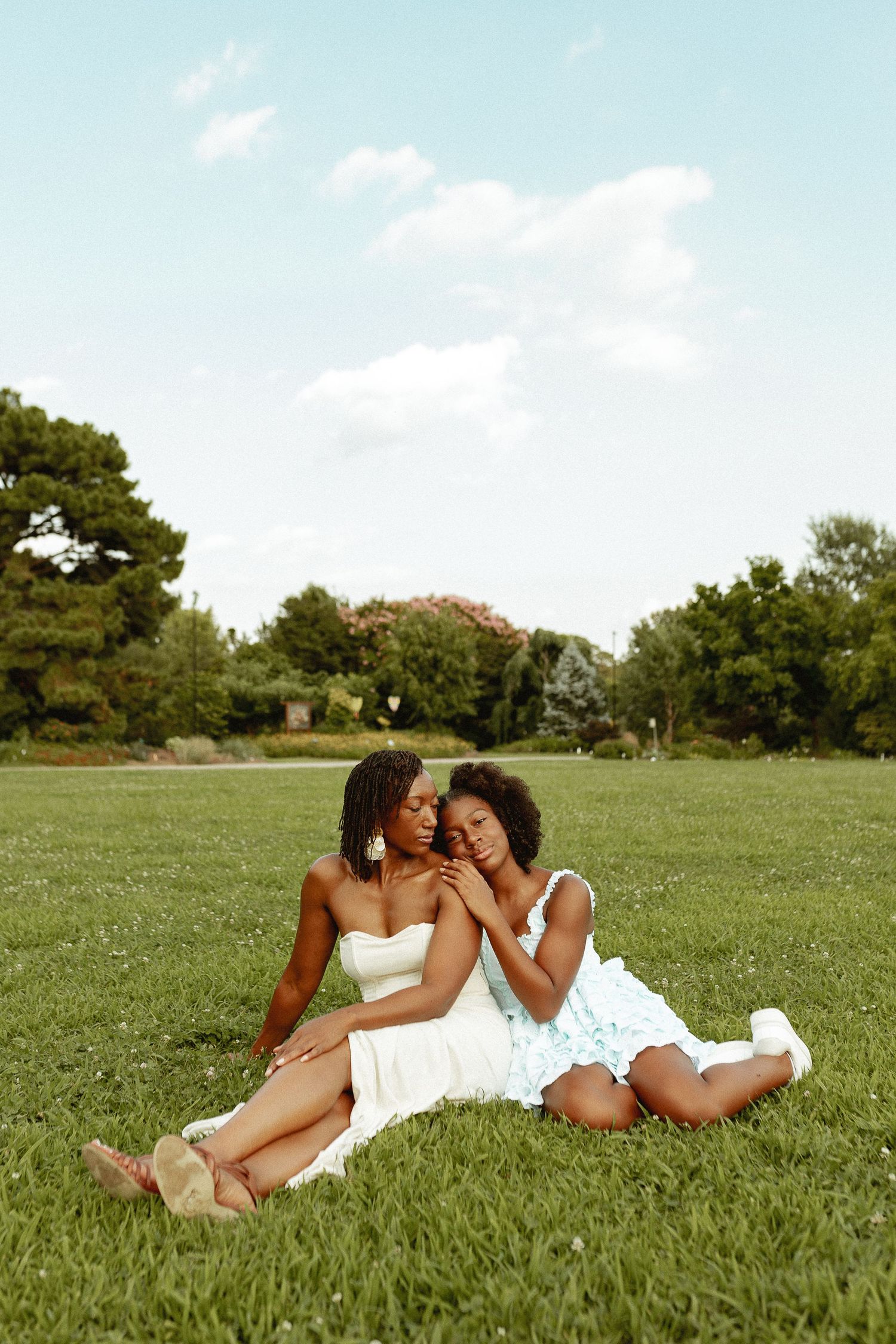 Two people in white dresses lying on grass taking photos of each other.