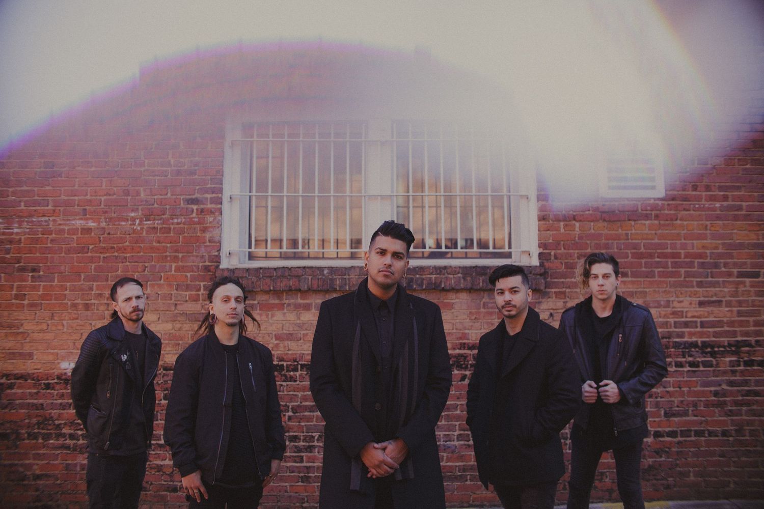 Band members posed against a brick wall in dark clothing.