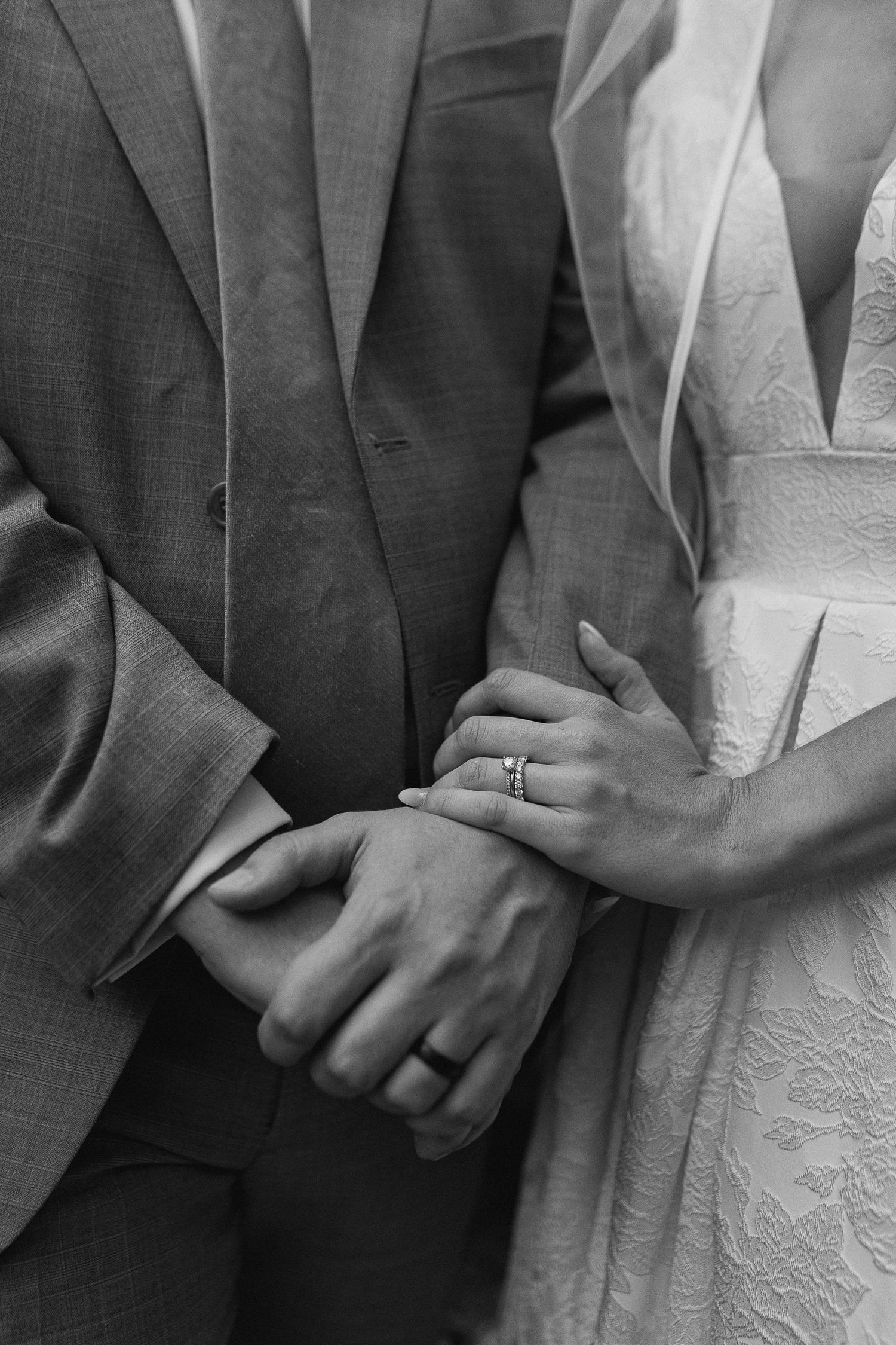 Black and white close-up of newlyweds holding hands showing wedding rings.