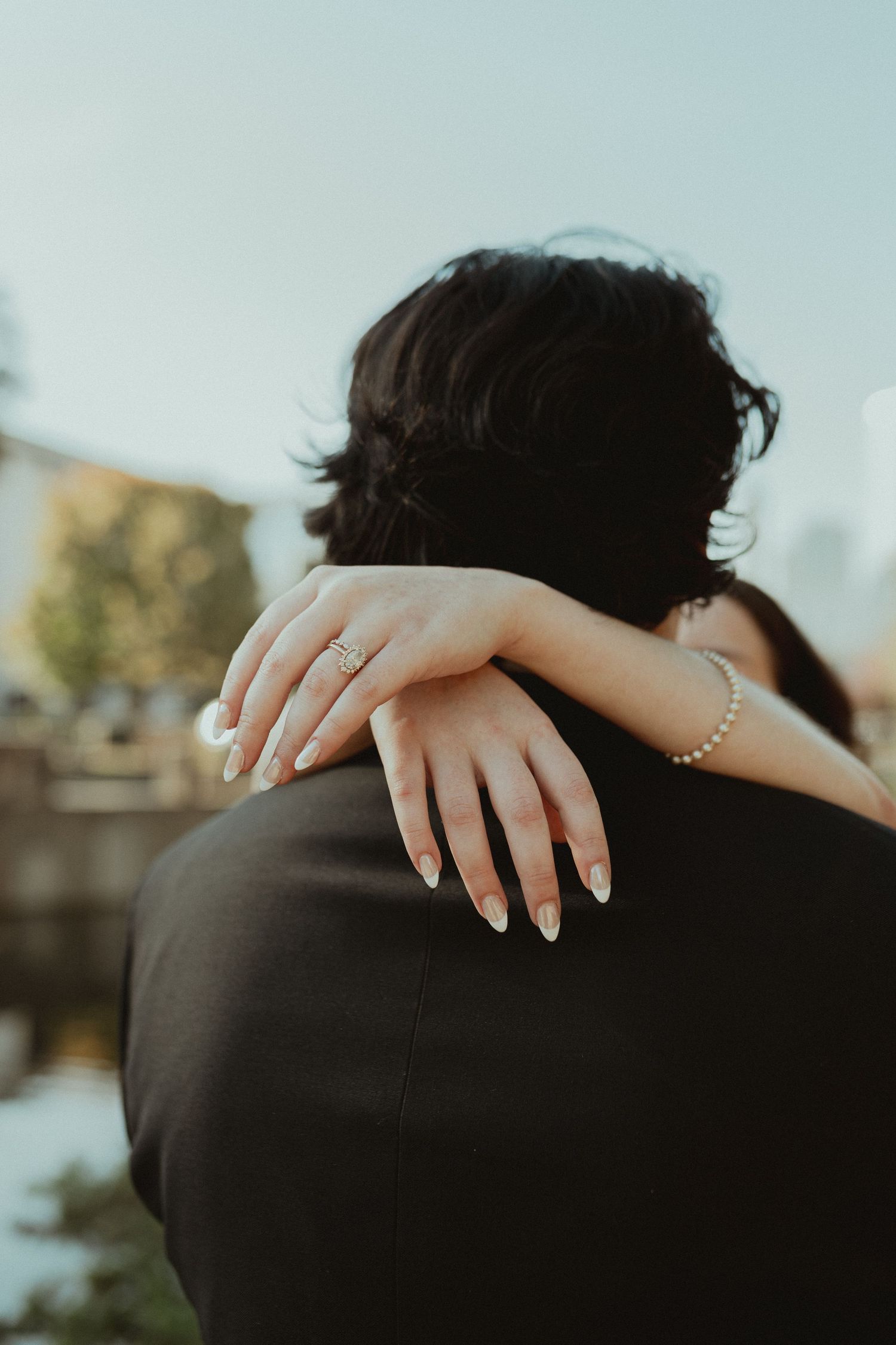 Manicured hands with an engagement ring embrace during an intimate moment.