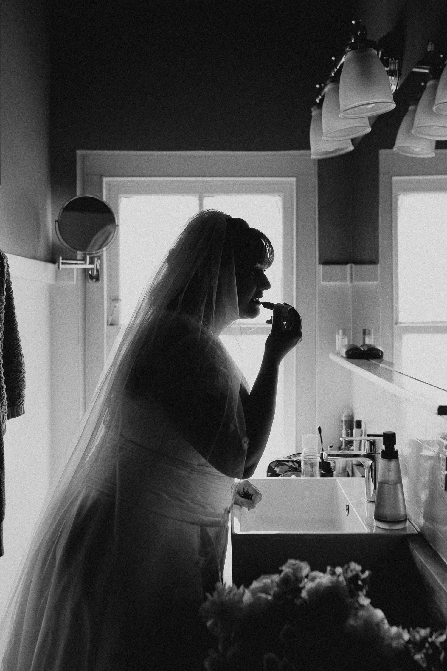 Silhouette of bride getting ready by window in dramatic black and white photography.