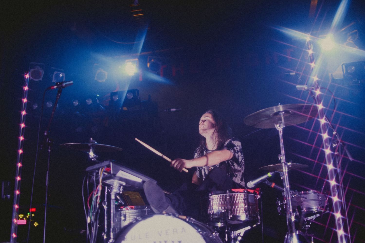 Concert performance with dramatic blue stage lighting and drum kit in focus.