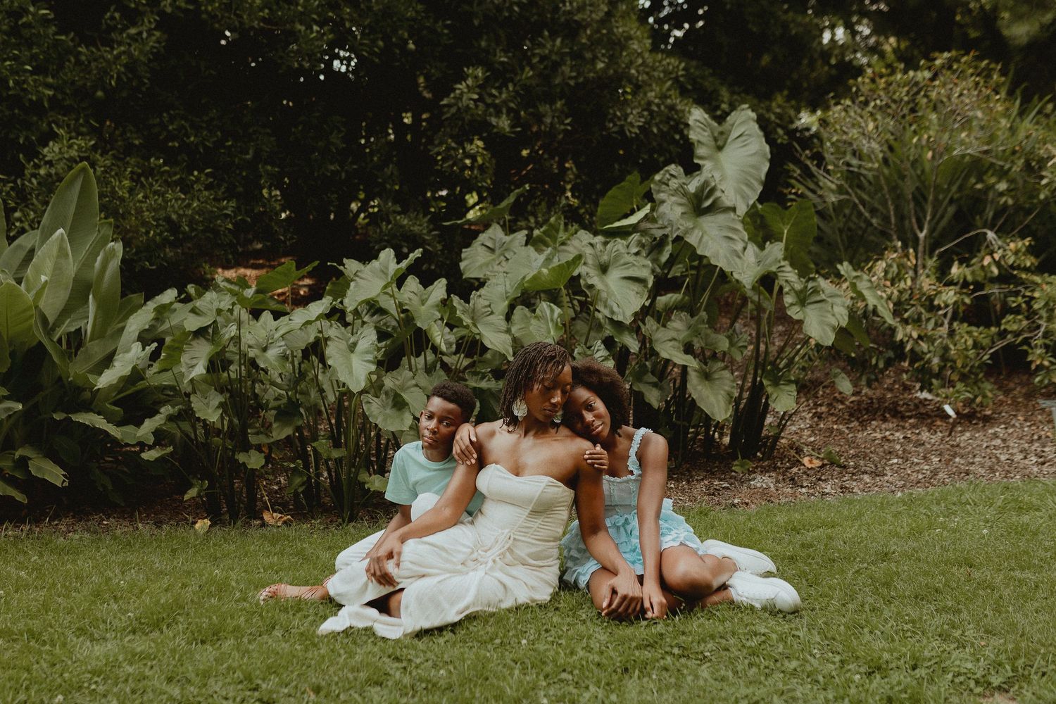 A group relaxing together on grass near lush green foliage on a summer day.