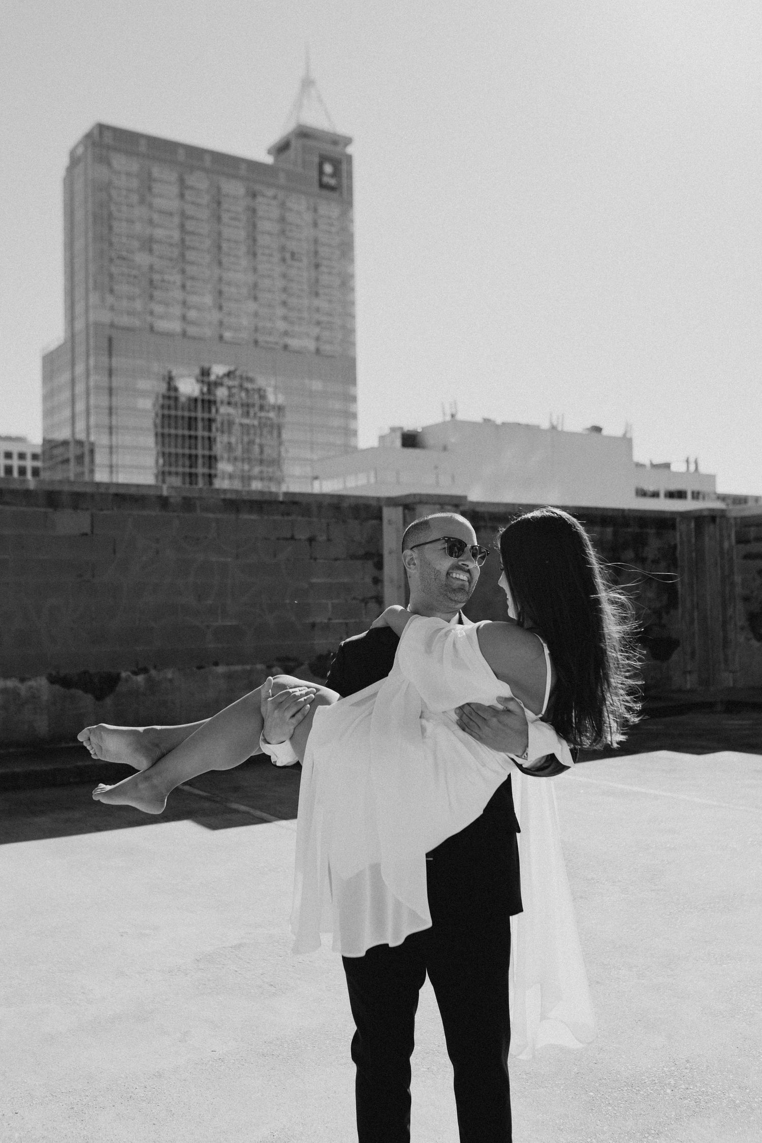 Couple in black and white stands against urban rooftop with dramatic pose.